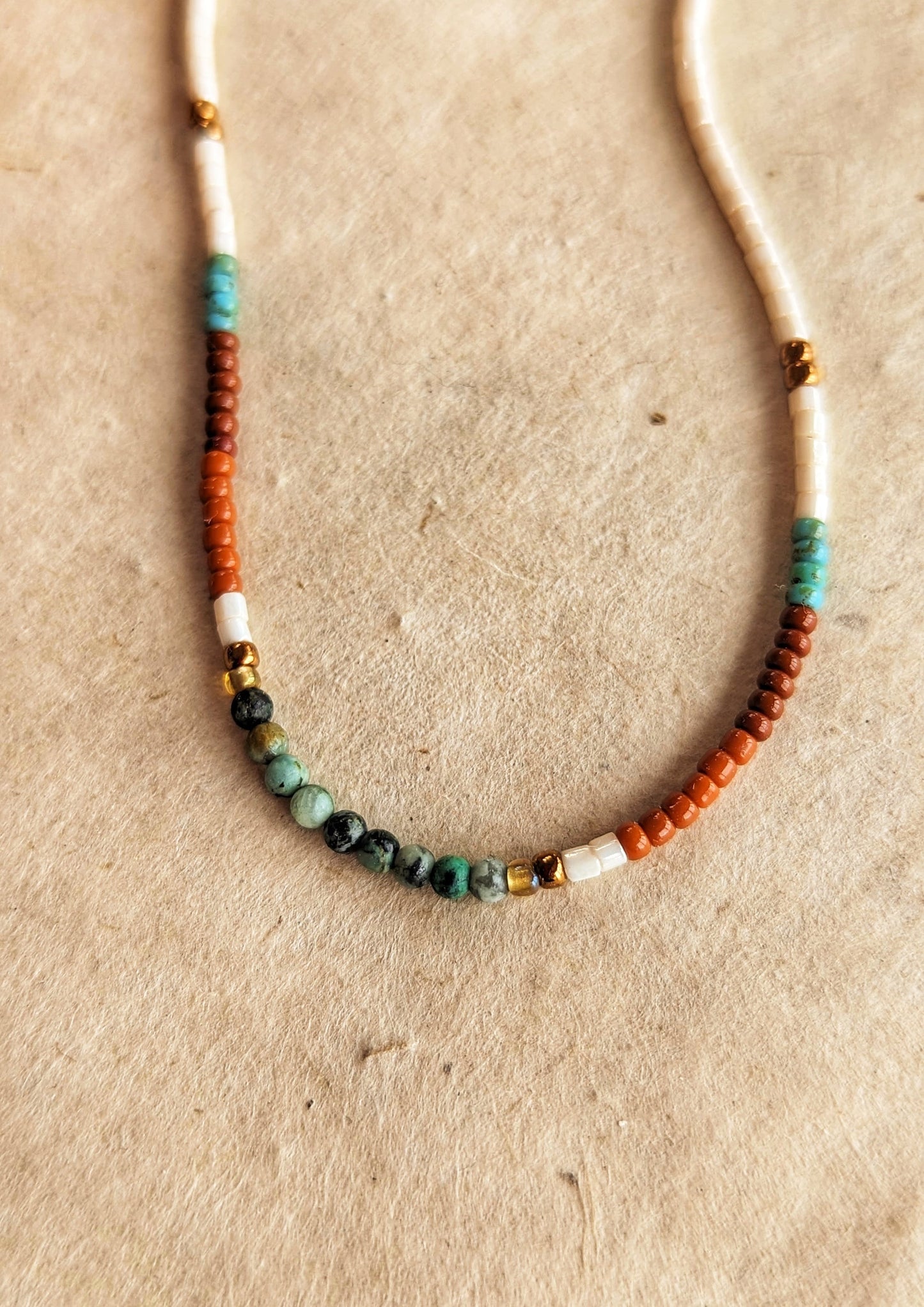 Moon & Milk handcrafted beaded choker necklace with ivory, terracotta, turquoise, and bronze beads in a simple pattern. Photographed on a beige background, showcasing its unique beadwork.