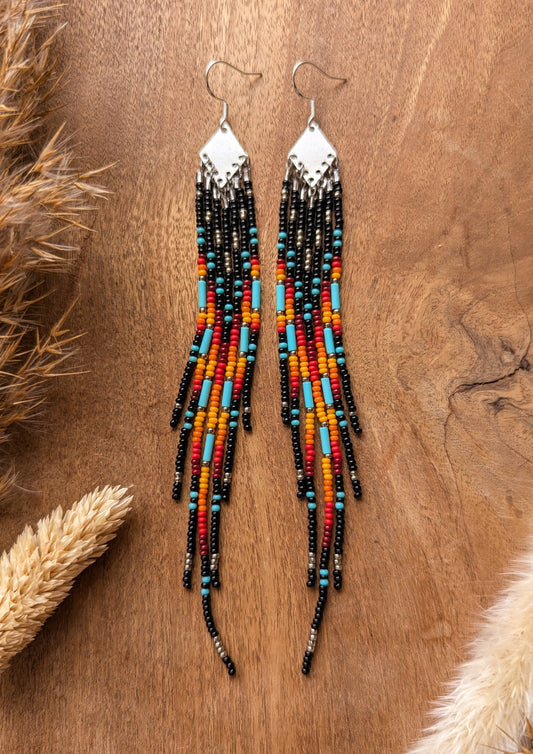 Handcrafted beaded earrings with a vibrant fringe design. The beads feature a bold mix of black, red, yellow, turquoise, and metallic accents, creating a striking, colorful pattern.