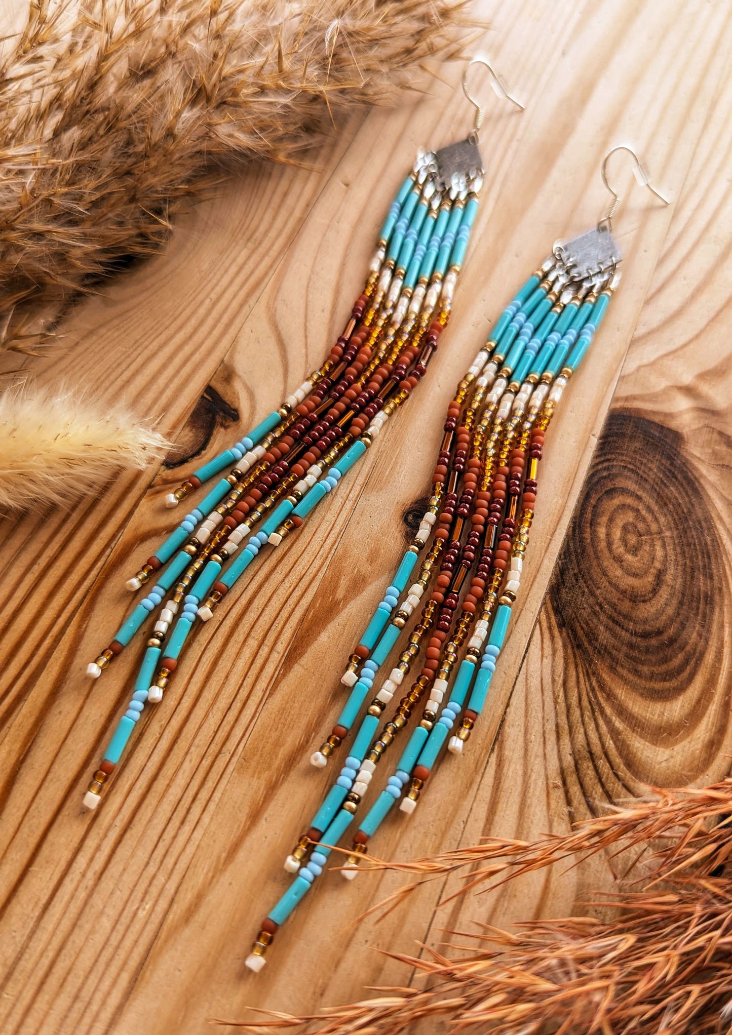 Long beaded earrings with turquoise, brown, and gold accents displayed on a wooden background.- Moon & Milk