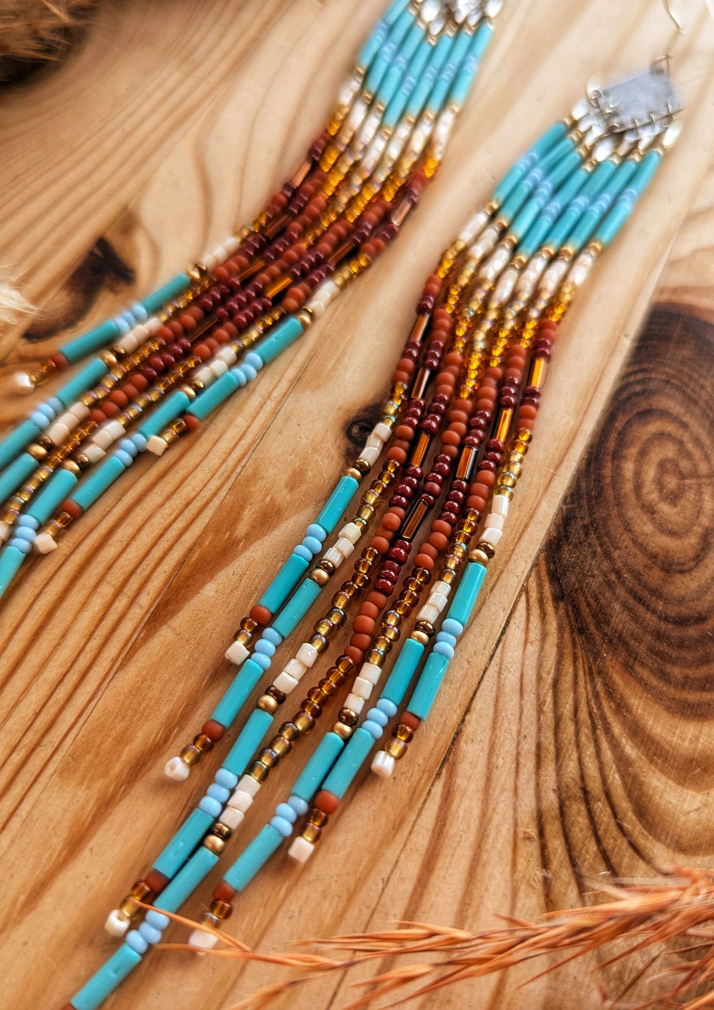 Long beaded earrings with turquoise, brown, and gold accents displayed on a wooden background.- Moon & Milk