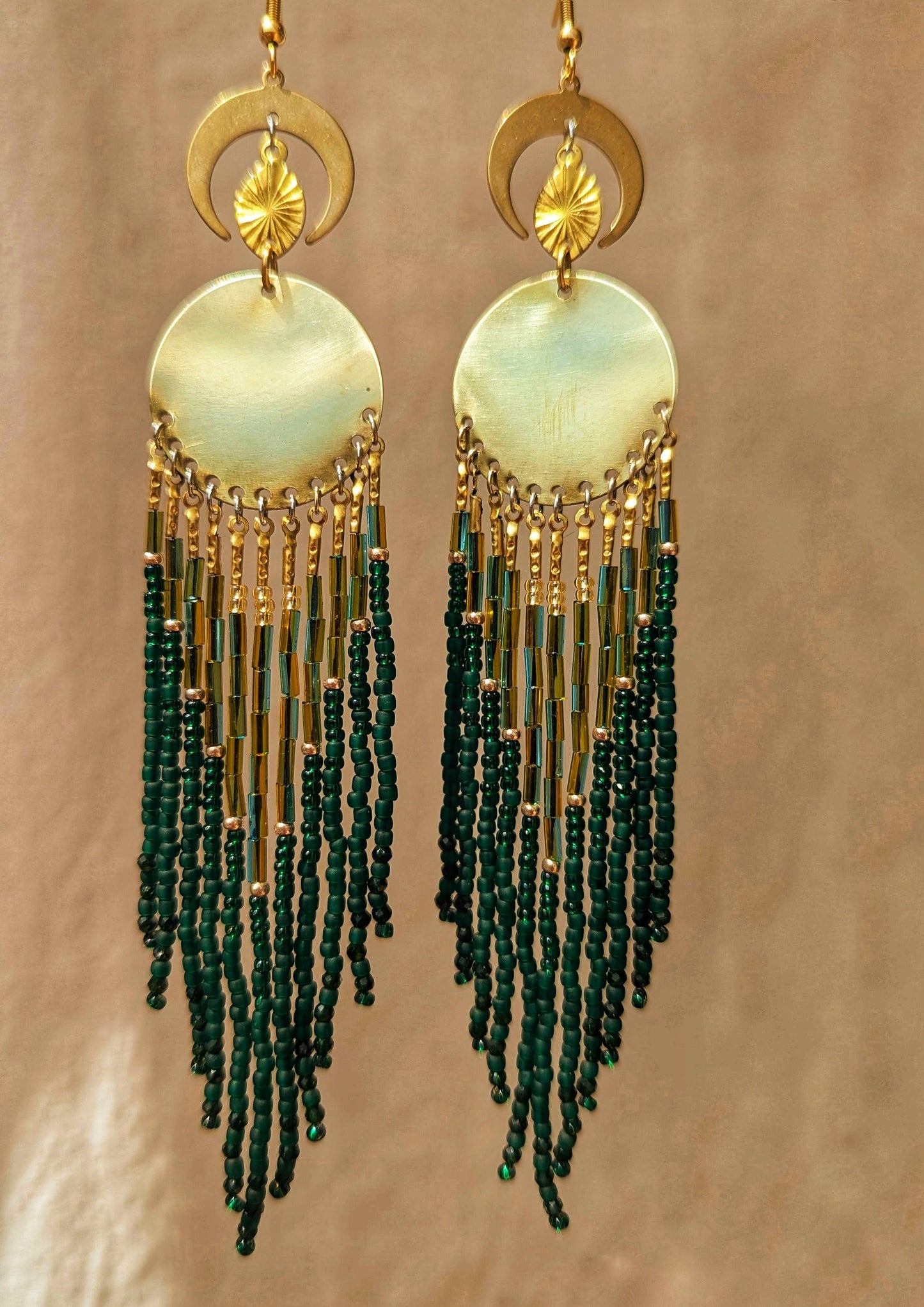 Elegant beaded earrings featuring a blend of green and gold beads, hanging from a round, brass centerpiece with crescent moon accents above. - Moon & Milk