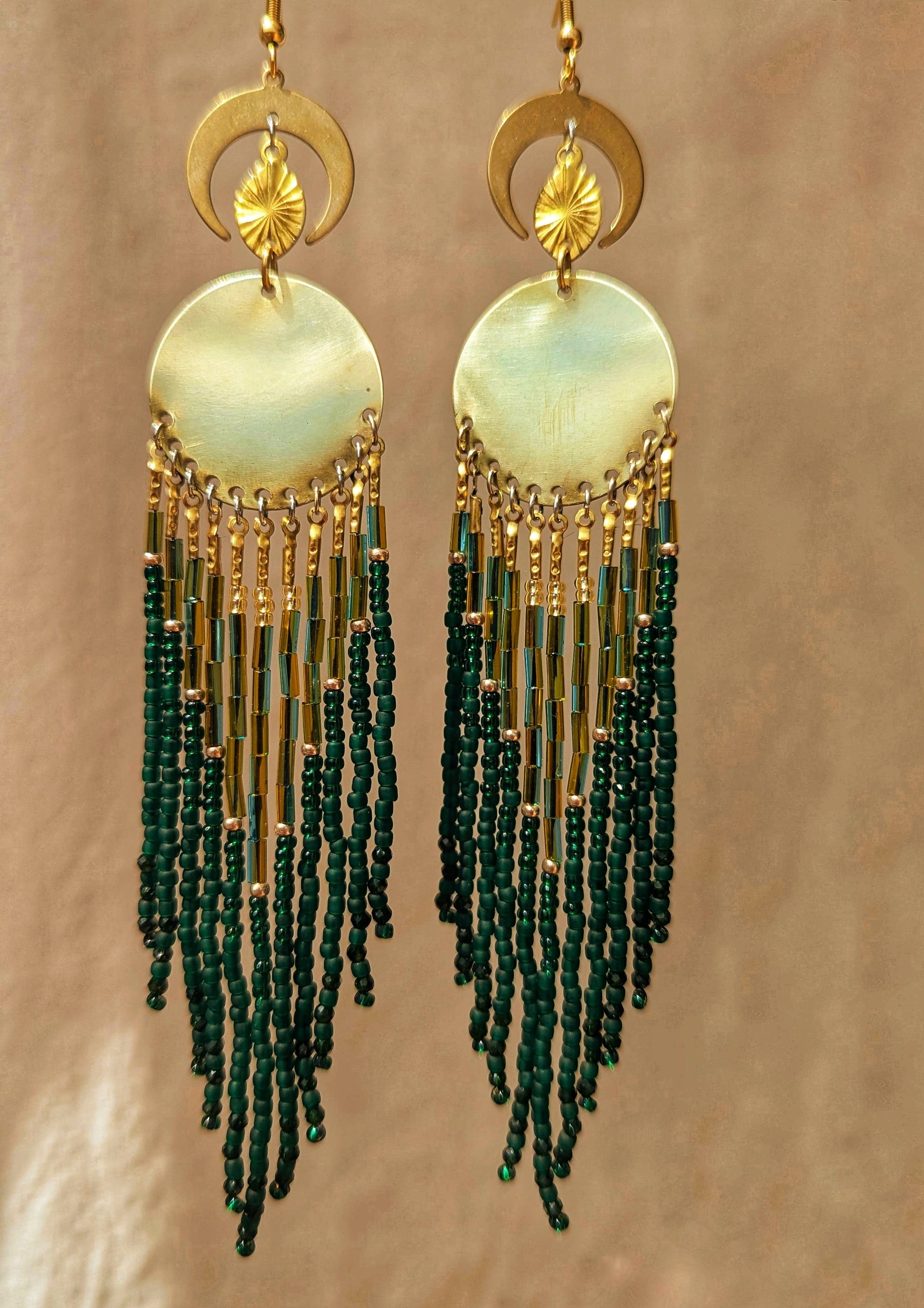Elegant beaded earrings featuring a blend of green and gold beads, hanging from a round, brass centerpiece with crescent moon accents above. - Moon & Milk