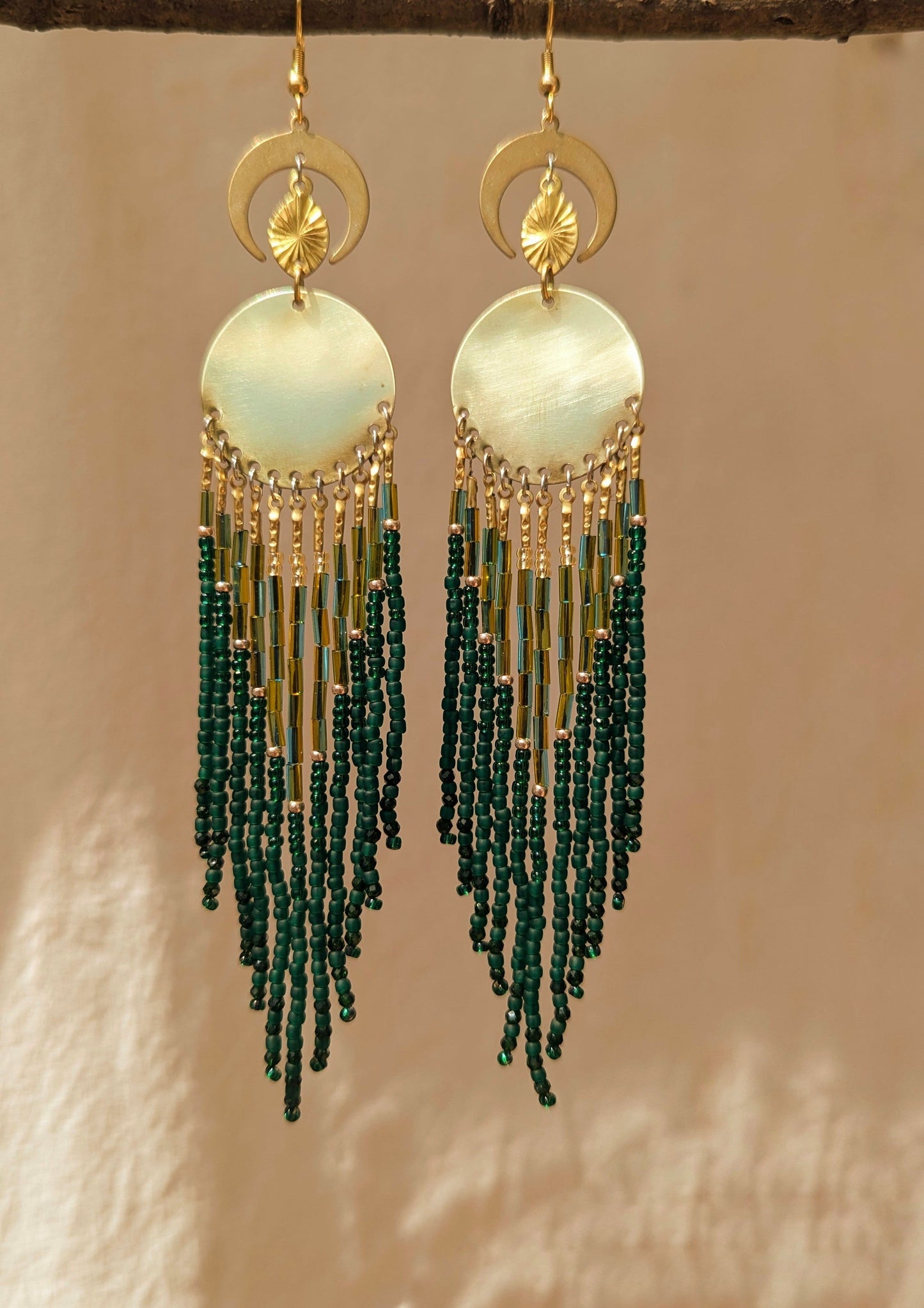 Elegant beaded earrings featuring a blend of green and gold beads, hanging from a round, brass centerpiece with crescent moon accents above. - Moon & Milk