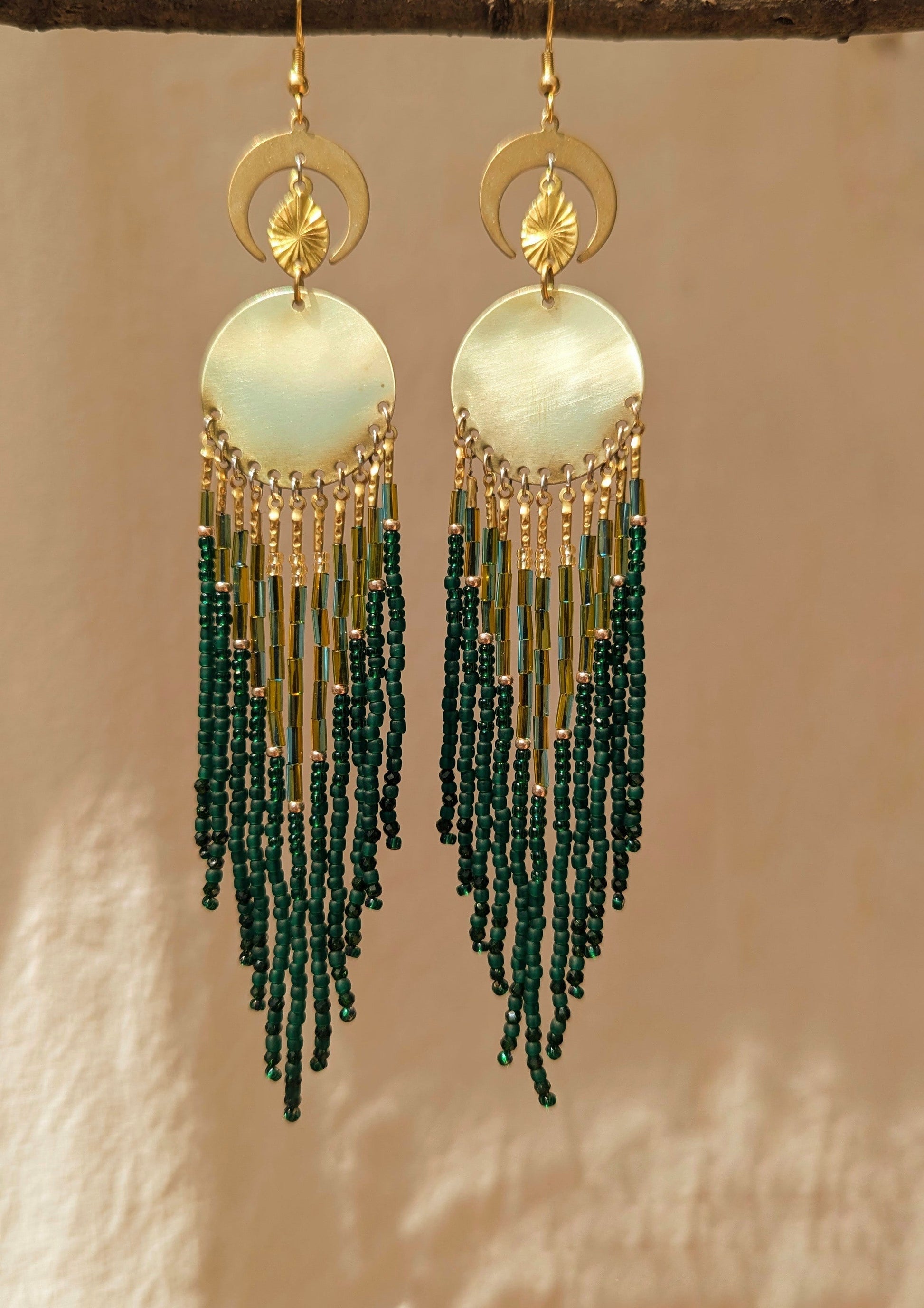 Elegant beaded earrings featuring a blend of green and gold beads, hanging from a round, brass centerpiece with crescent moon accents above. - Moon & Milk