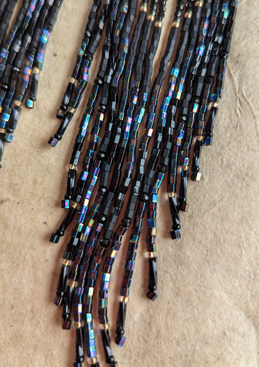 Close-up of Moon & Milk handcrafted beaded earrings with black beads, brass crescent tops, and long flowing strands in a boho, fringe-style design.