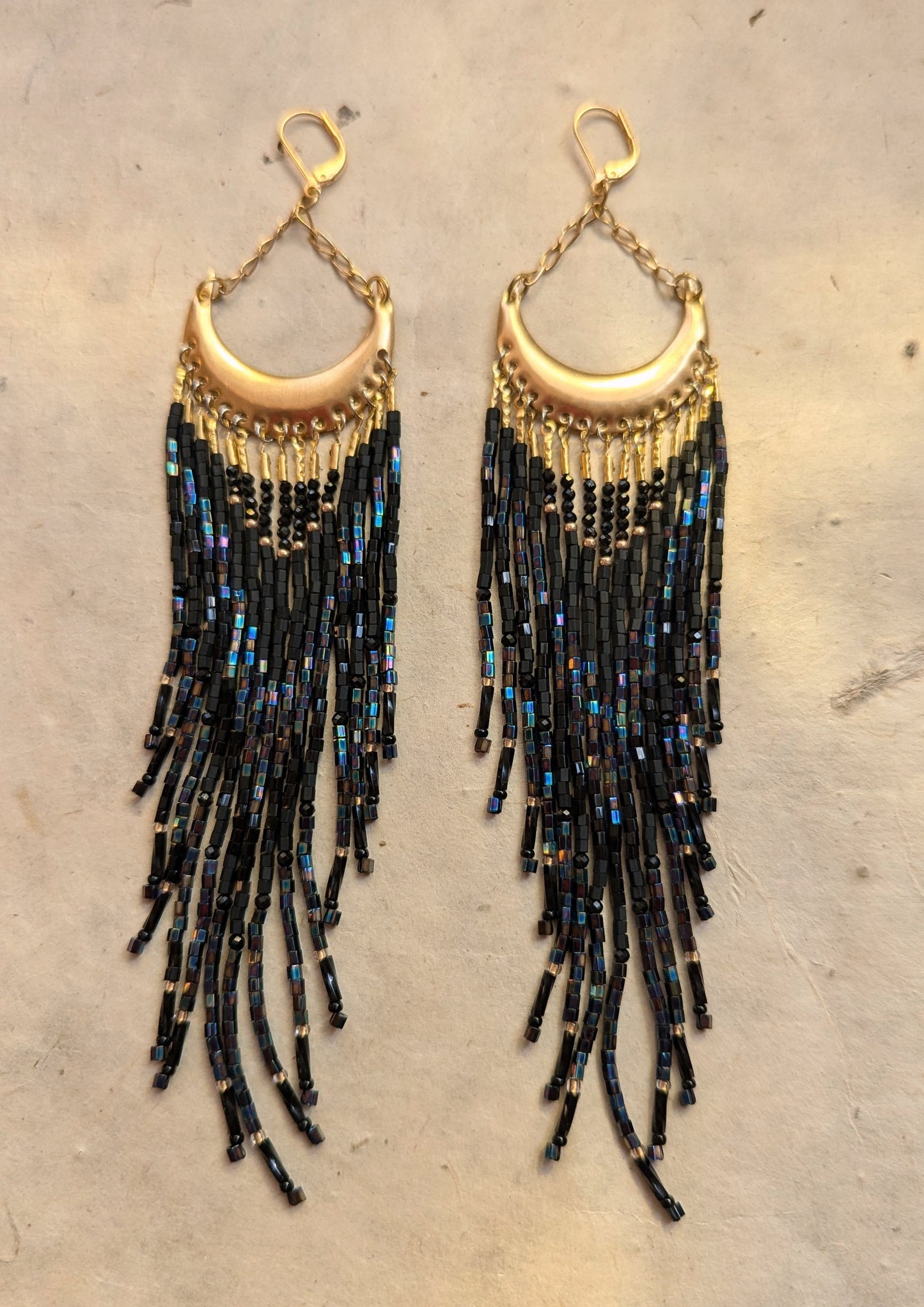 Moon & Milk handcrafted beaded earrings with black beads, brass crescent tops, and long flowing strands in a boho, fringe-style design.