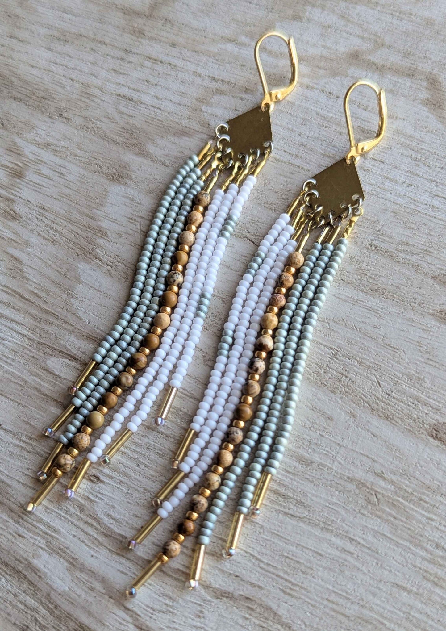 White beaded earrings with jasper stones and gold accents on a wooden surface.