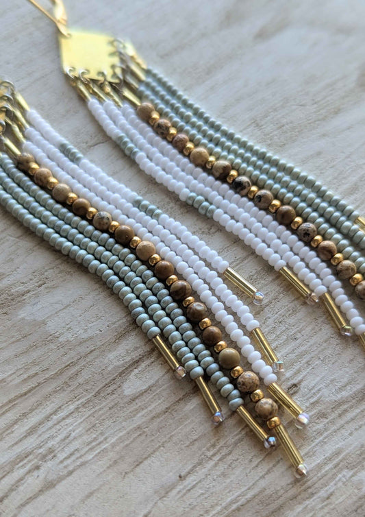 Multistrand beaded earrings with gold accents on a light wooden surface.