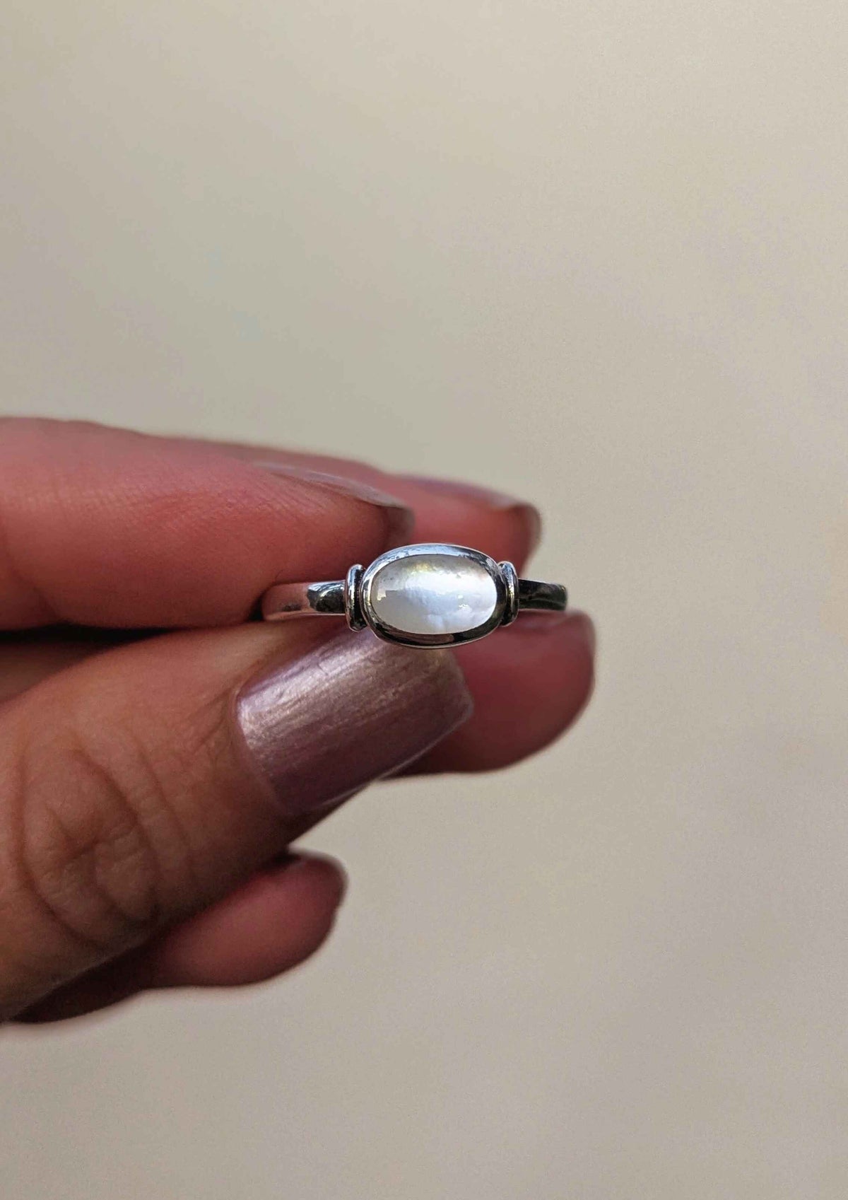 Silver ring with a mother of pearl in the center held between fingers against a plain background.