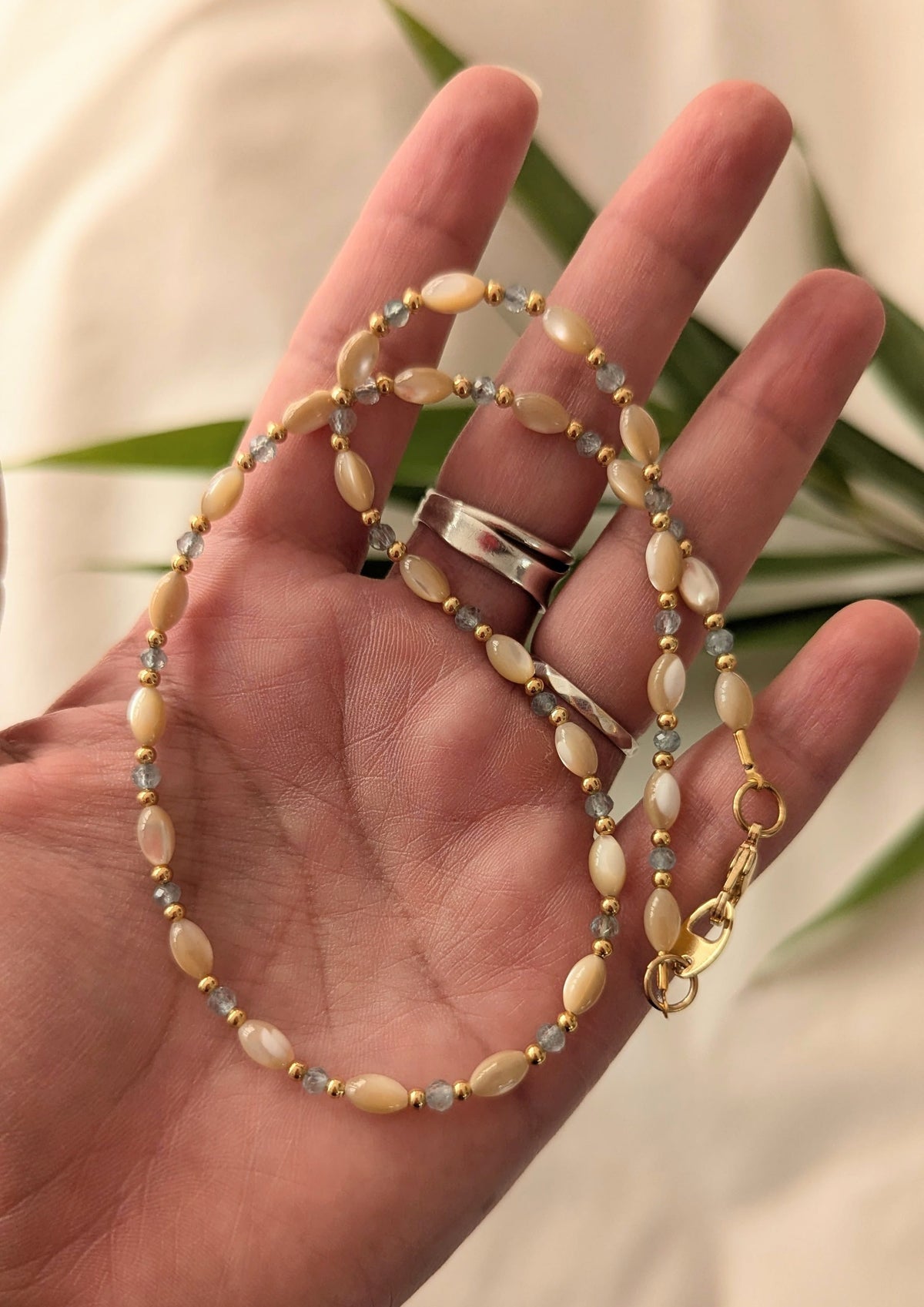 Hand holding a mother-of-pearl beaded necklace with a blurred natural background.