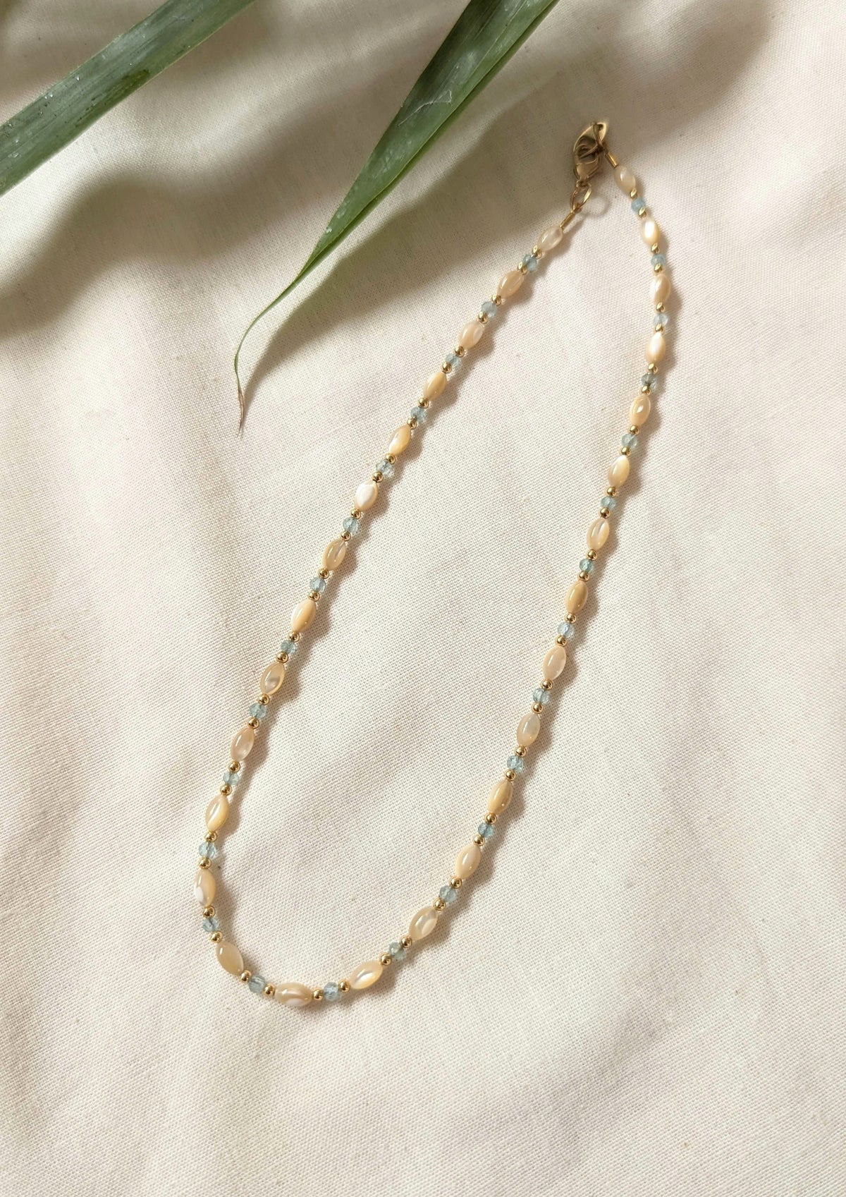 Mother of pearl necklace with mother-of-pearl rice beads on a beige fabric background.