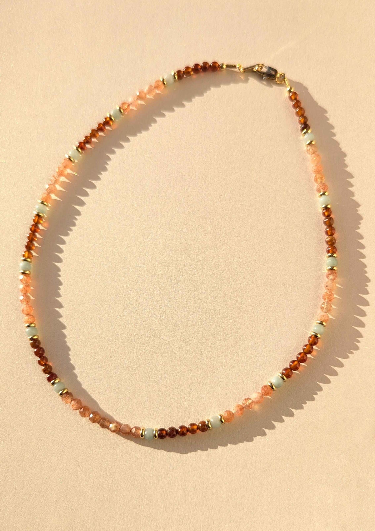 Gemstone necklace with orange sunstone and brown garnet beads on a beige background.