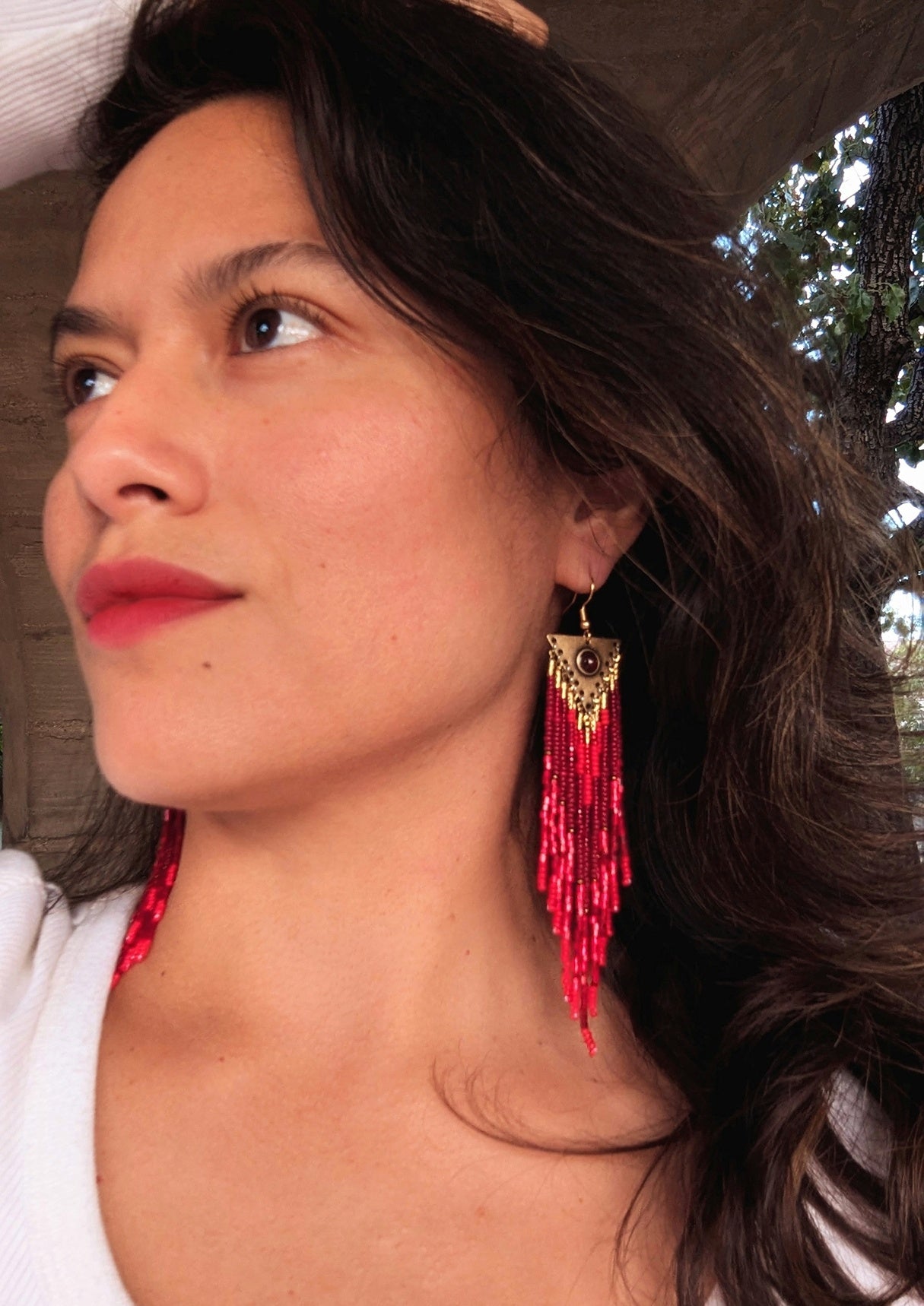 Handcrafted beaded earrings on a model by Moon & Milk, featuring red Czech beads, brass accents, and a garnet centerpiece, showcasing intricate beadwork and artistic design.