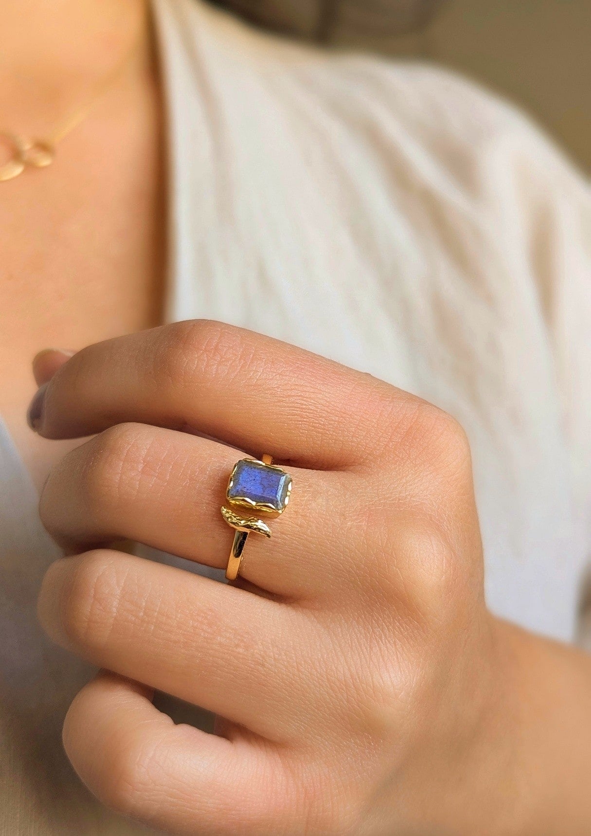 Gold-plated ring with a rectangular labradorite stone and a sculpted branch detail, shown worn on a hand.