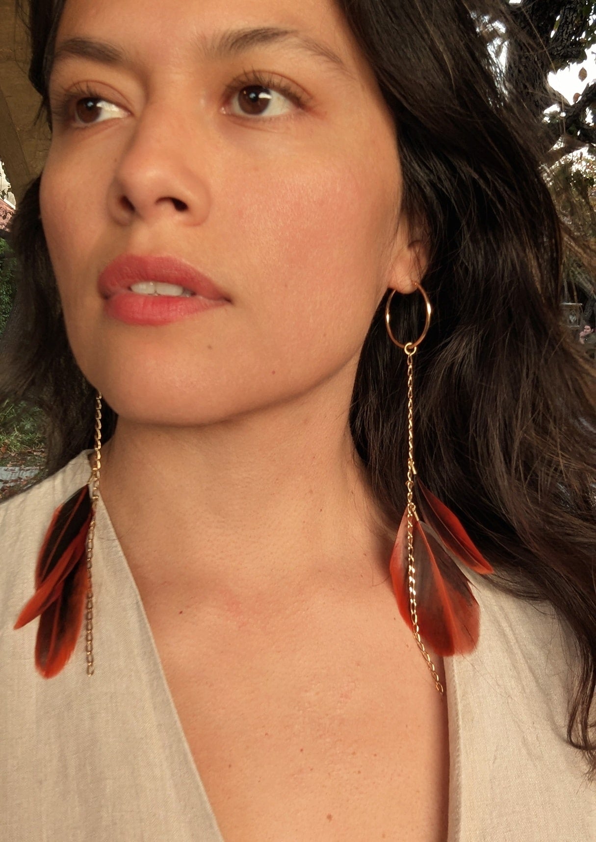 Moon & Milk feather hoop earrings with orange and brown tones on gold hoops,  modeled by a woman outdoors.