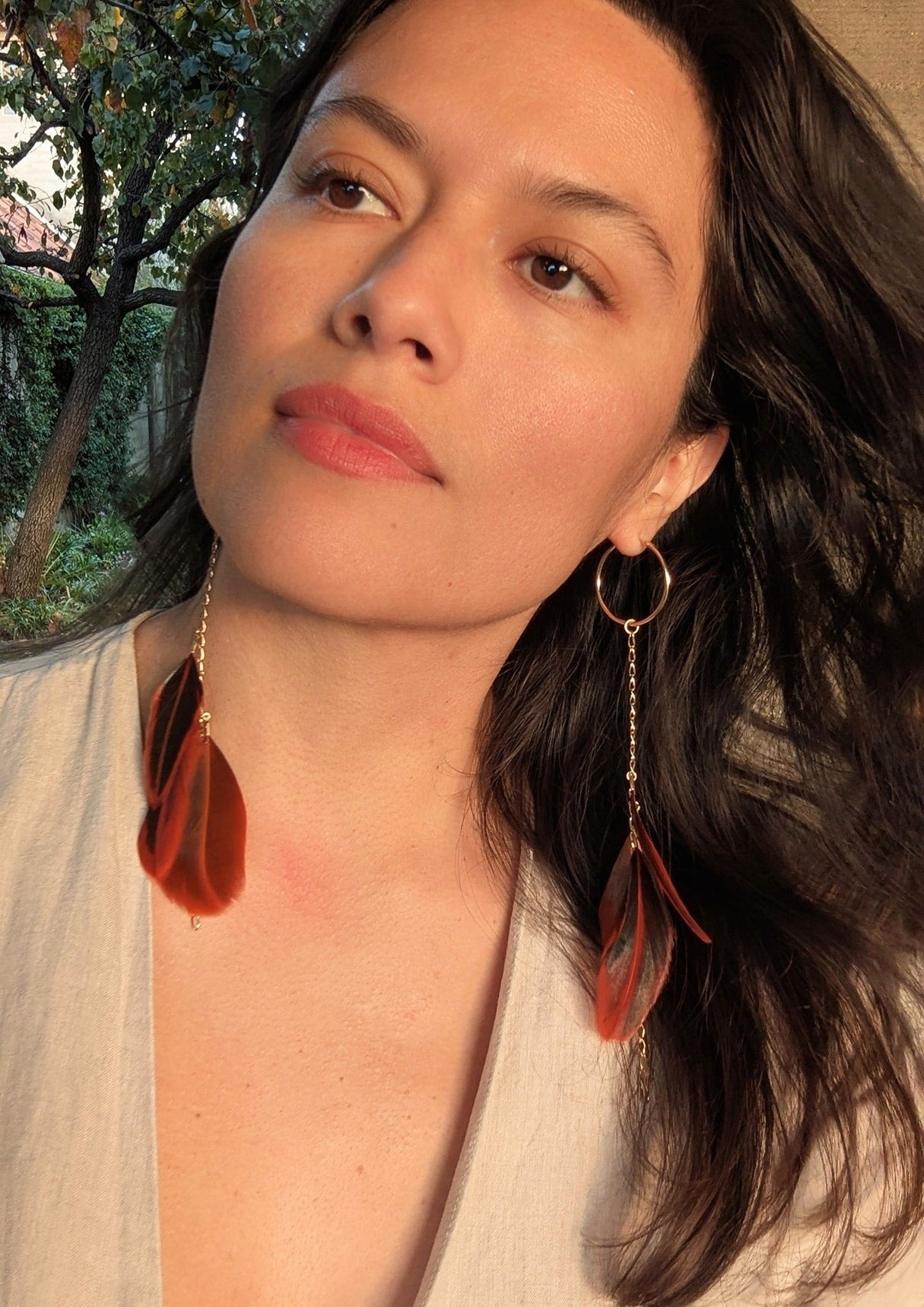 Moon & Milk feather hoop earrings with orange and brown tones on gold hoops,  modeled by a woman outdoors.