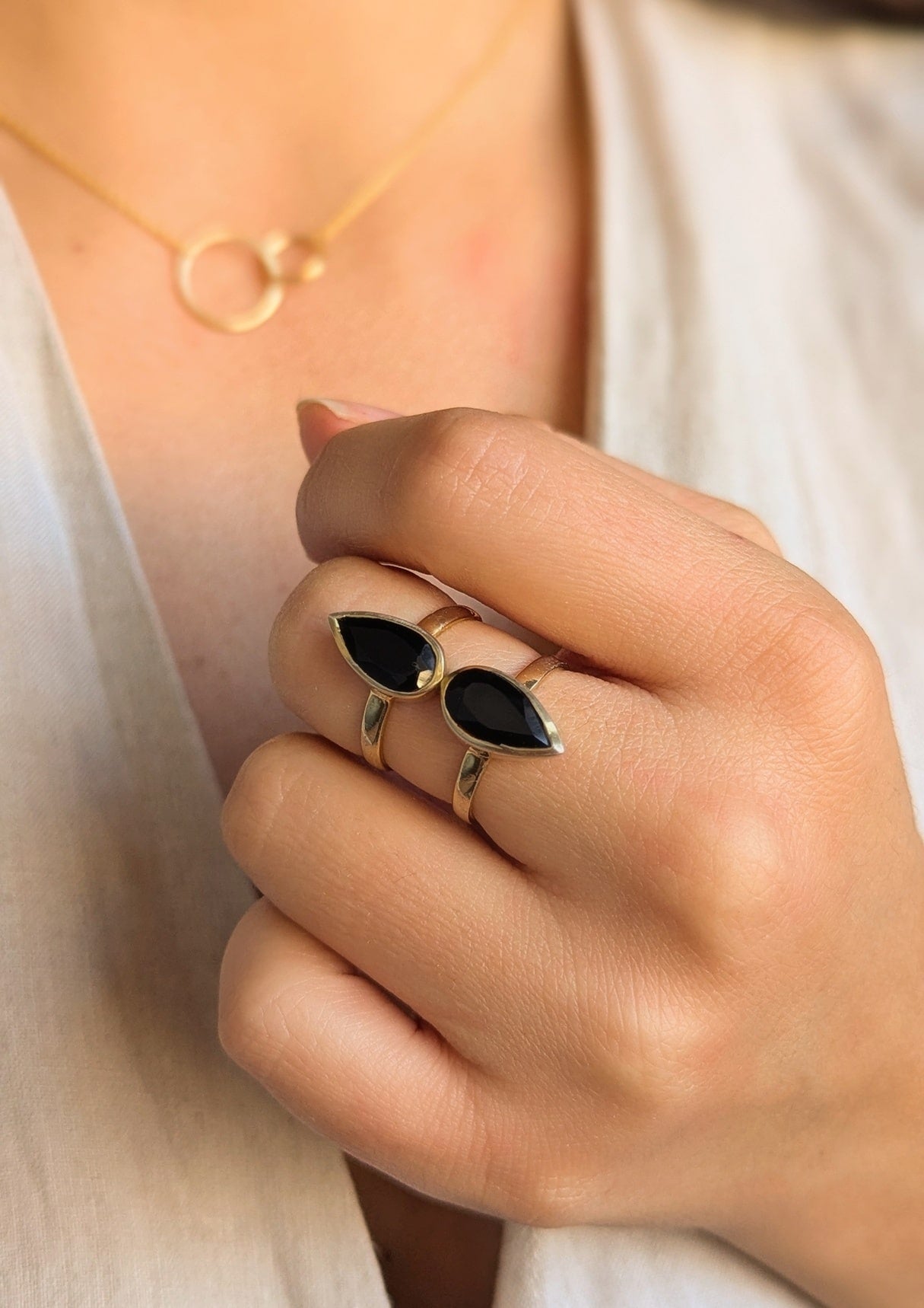 Hand wearing a gold ring with two teardrop-shaped black onyx stones, paired with a delicate gold circle necklace from Moon & Milk.