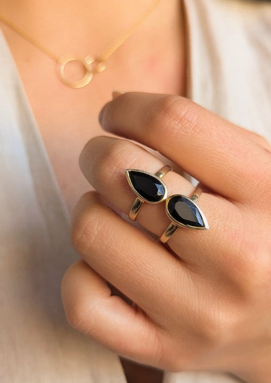 Hand wearing a gold ring with two teardrop-shaped black onyx stones, paired with a delicate gold circle necklace from Moon & Milk.