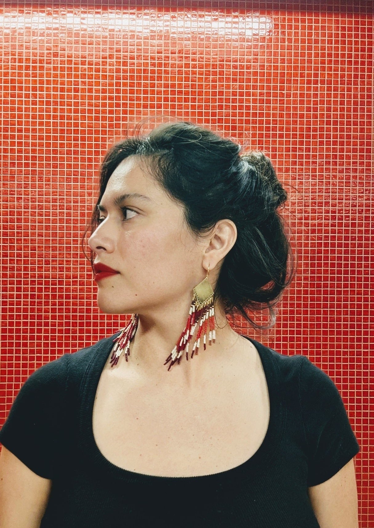 Moon & Milk handmade beaded earrings with burgundy, white, and red beadwork in chevron patterns hanging from brass diamond tops, worn by a woman.