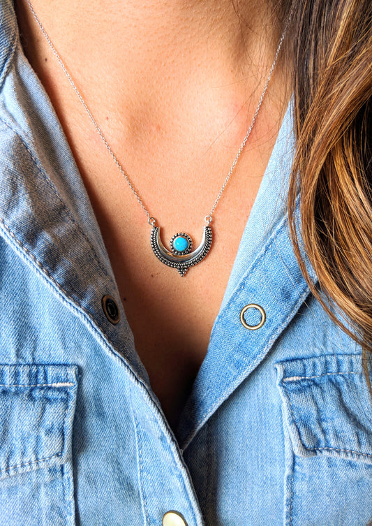 A crescent moon pendant necklace on a model with a round turquoise stone bezel setting and a silver chain. -Moon & Milk