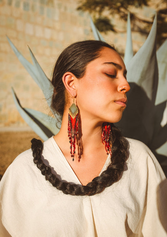 Woman wearing red beaded earrings with a blurred natural background.
