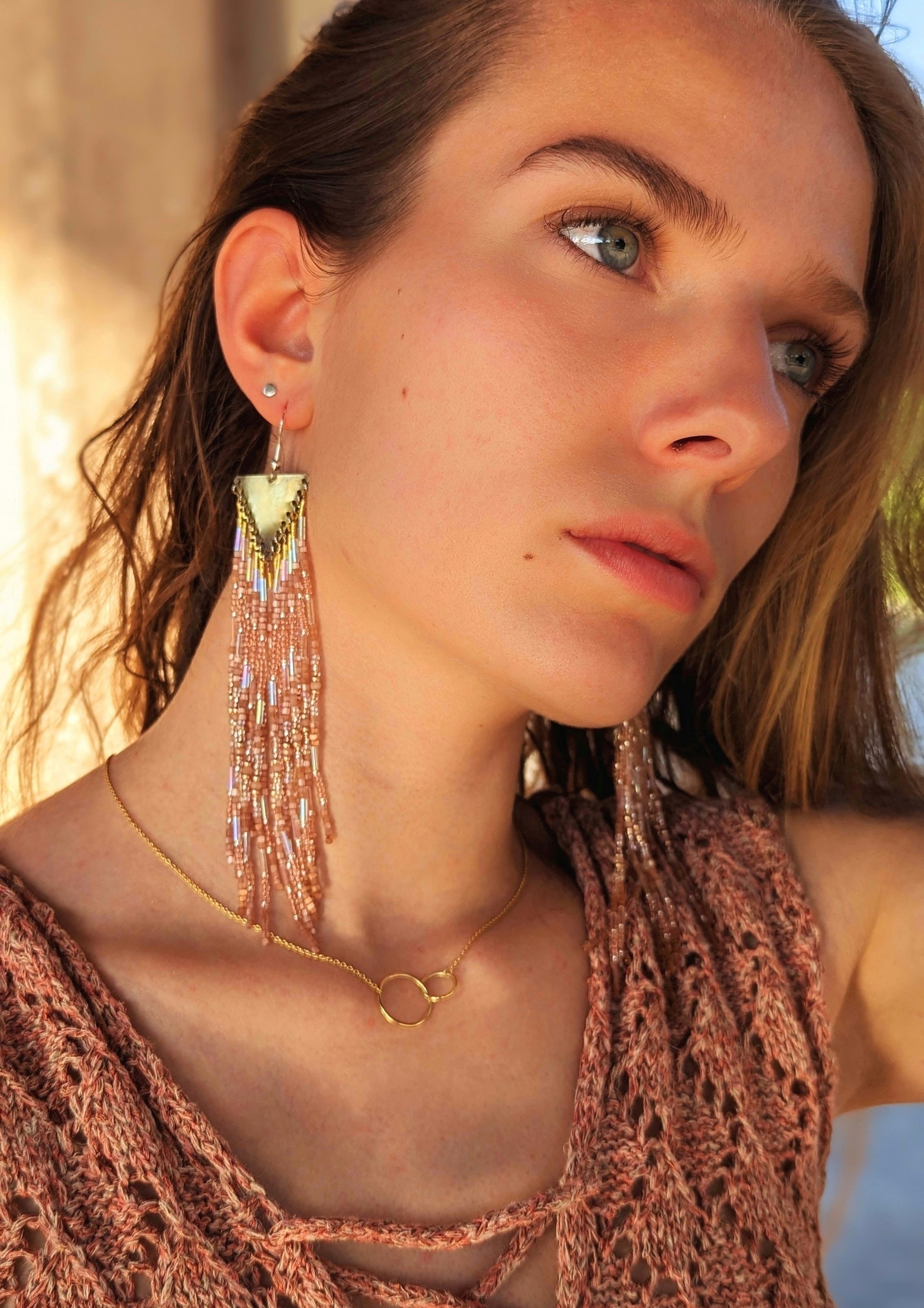 Model wearing Moon & Milk long beaded earrings in warm bronze and peach tones with brass findings, styled with a gold necklace in natural light.