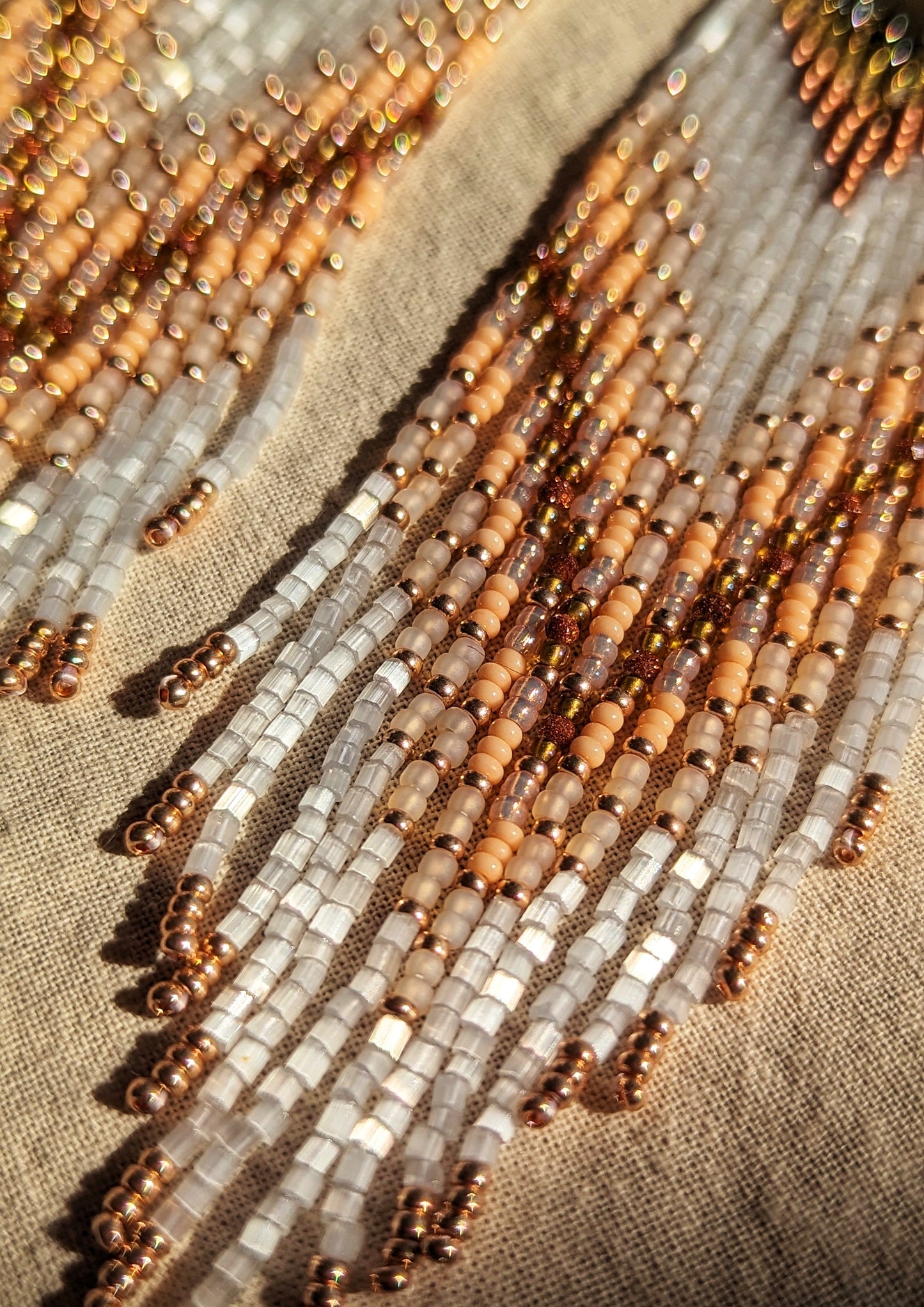 An elegant close-up of delicate beadwork with warm beige, white, and rose gold tones, showcasing a subtle shimmer under natural light. Perfectly captures the intricate craftsmanship and texture of these statement earrings. - Moon & Milk