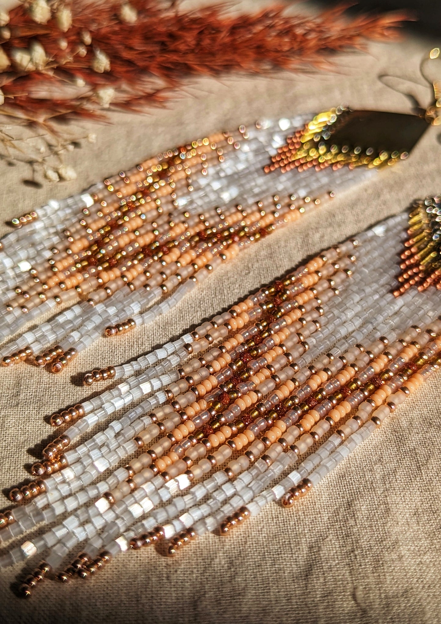 An elegant close-up of delicate beadwork with warm beige, white, and rose gold tones, showcasing a subtle shimmer under natural light. Perfectly captures the intricate craftsmanship and texture of these statement earrings. - Moon & Milk
