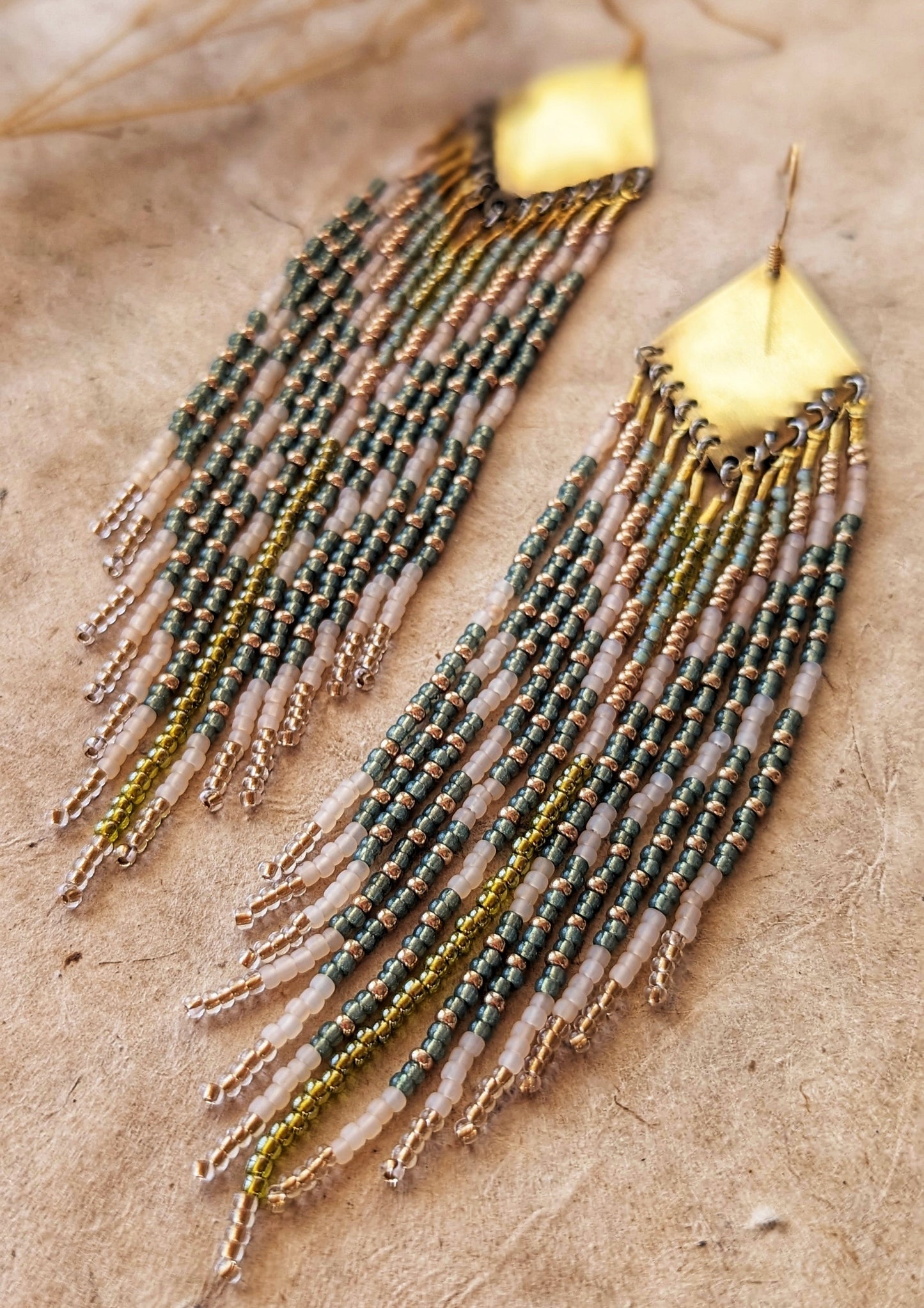 Moon & Milk green, gold, and cream beaded earrings on brass findings, laid on linen with dried flowers and a natural background.