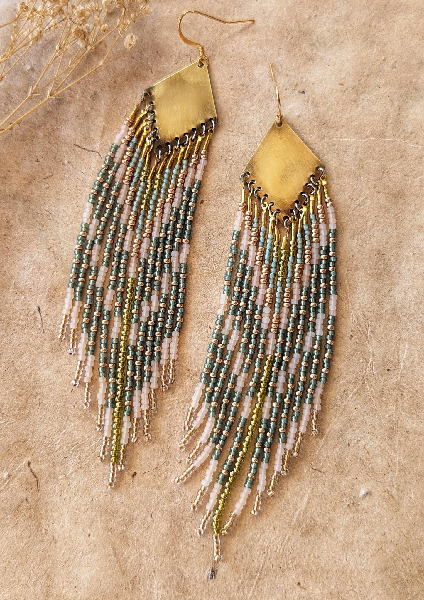 Moon & Milk green, gold, and cream beaded earrings on brass findings, laid on linen with dried flowers and a natural background.