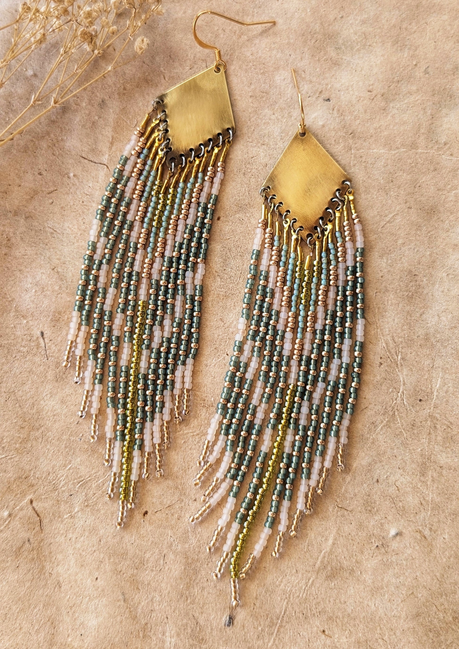 Moon & Milk green, gold, and cream beaded earrings on brass findings, laid on linen with dried flowers and a natural background.