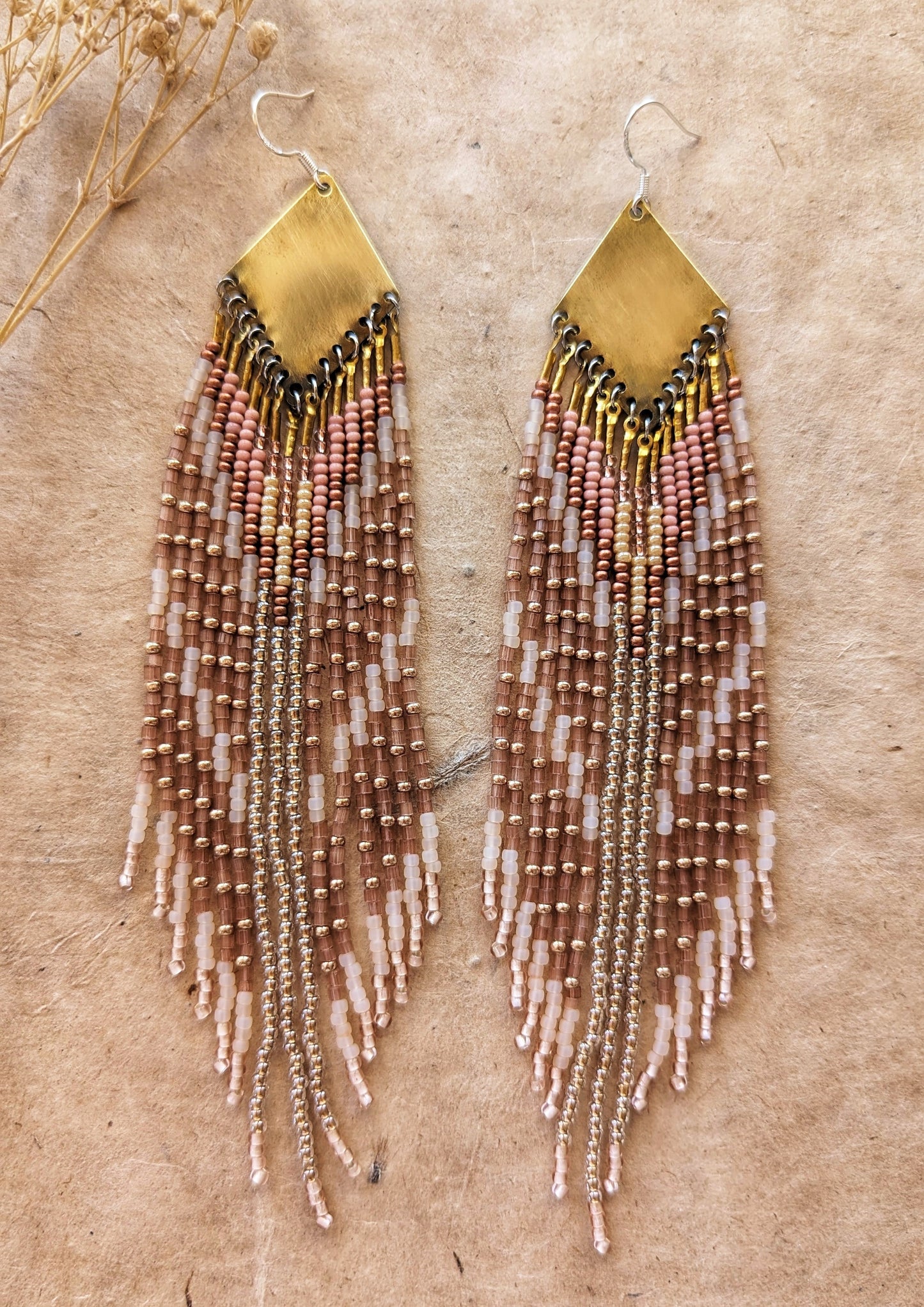 A pair of handcrafted seed bead earrings with a geometric pattern in gold and mauve colors, featuring brass accents and gold-plated ear wires.