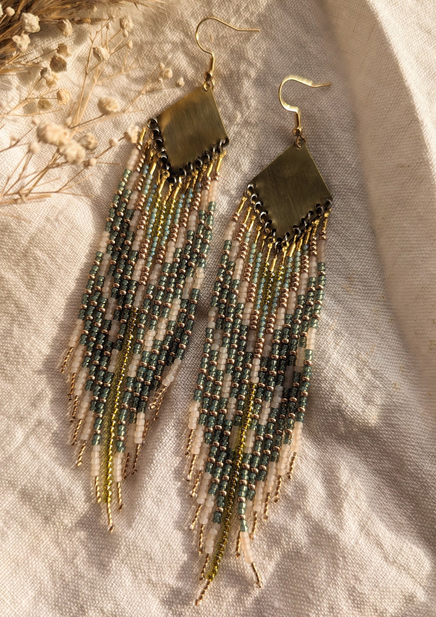 Moon & Milk green, gold, and cream beaded earrings on brass findings, laid on linen with dried flowers and soft natural light.