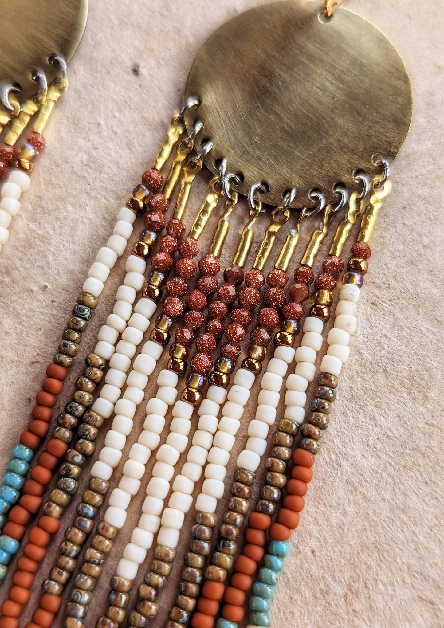 Gold dangling beaded earrings with earthy-toned beads in white, brown, and turquoise. Large circular brass discs at the top. Handcrafted by Moon & Milk.