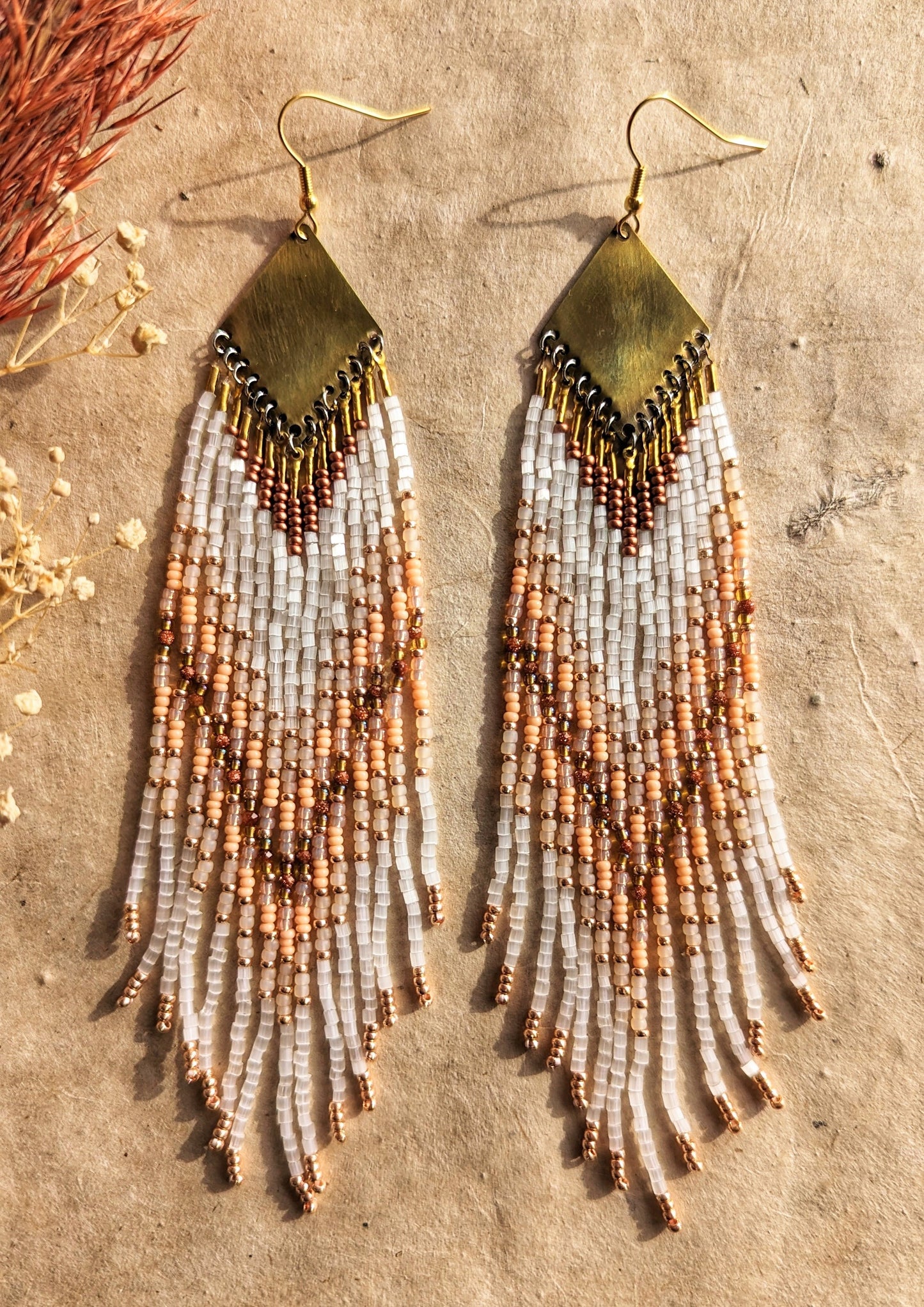 A beautifully textured close-up of beaded fringe earrings in white, beige, and rose gold tones, highlighting the artistry and detail in each strand. - Moon & Milk