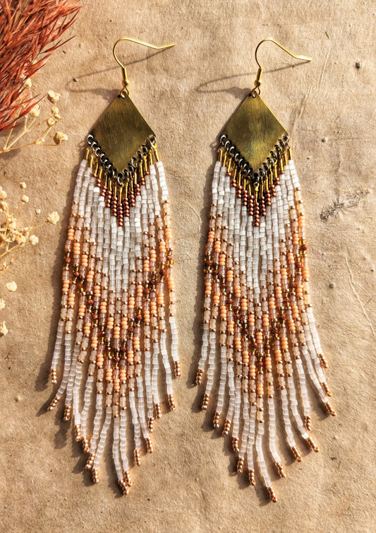 A beautifully textured close-up of beaded fringe earrings in white, beige, and rose gold tones, highlighting the artistry and detail in each strand. - Moon & Milk