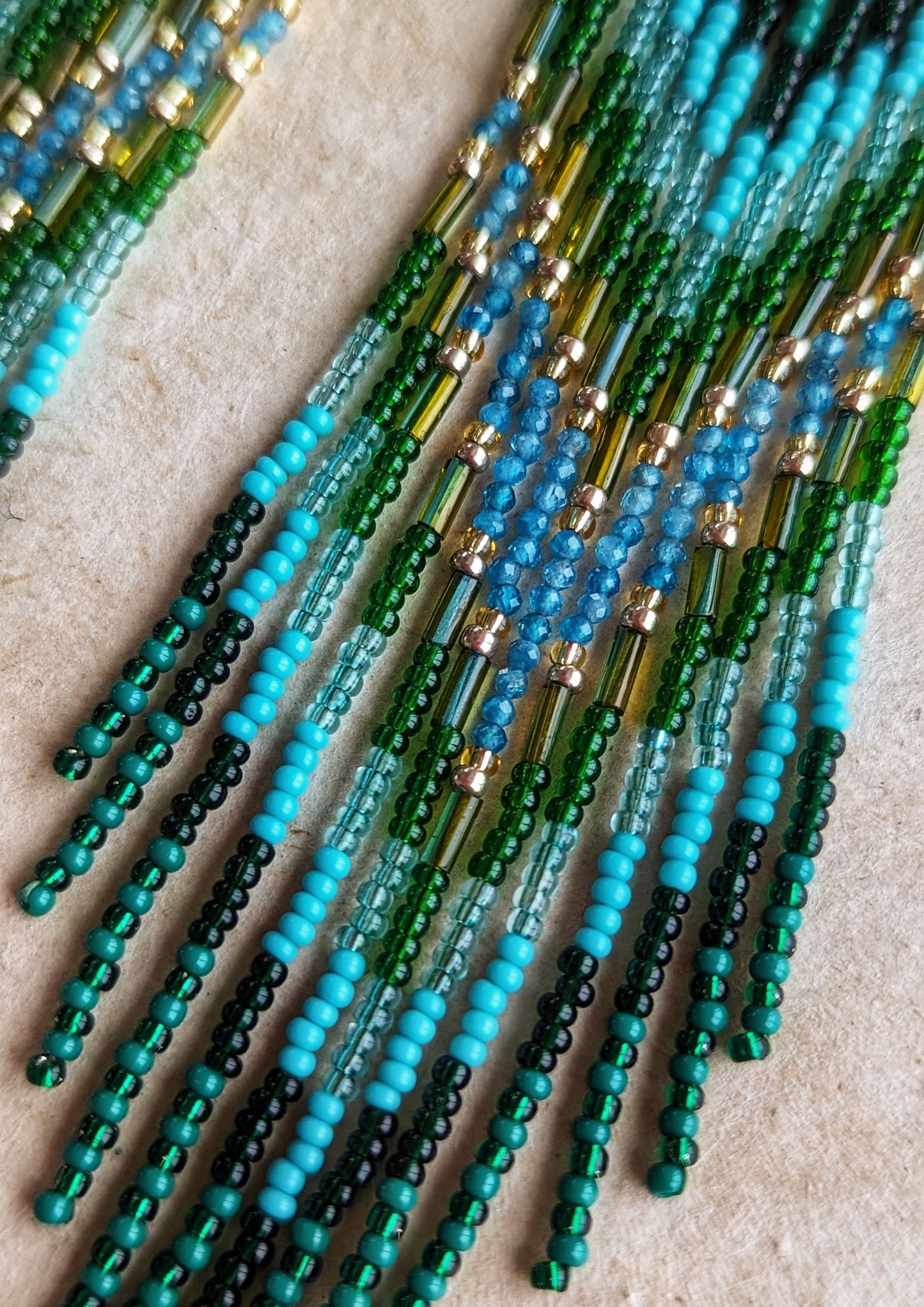 Close-up of long native earrings by Moon & Milk with turquoise, apatite, and green glass beads, featuring brass accents and intricate artisan beadwork.