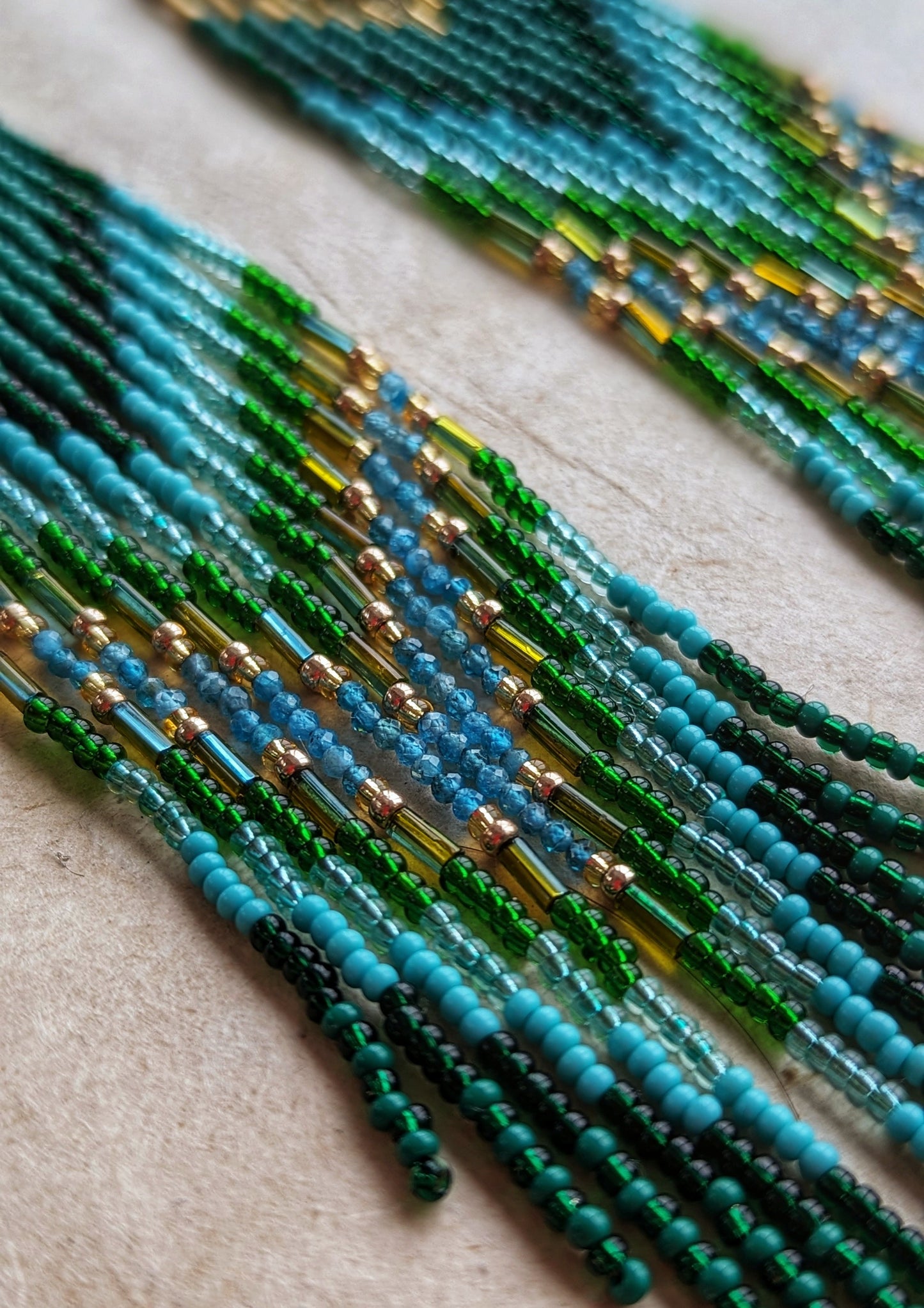 Close-up of long native earrings by Moon & Milk with turquoise, apatite, and green glass beads, featuring brass accents and intricate artisan beadwork.