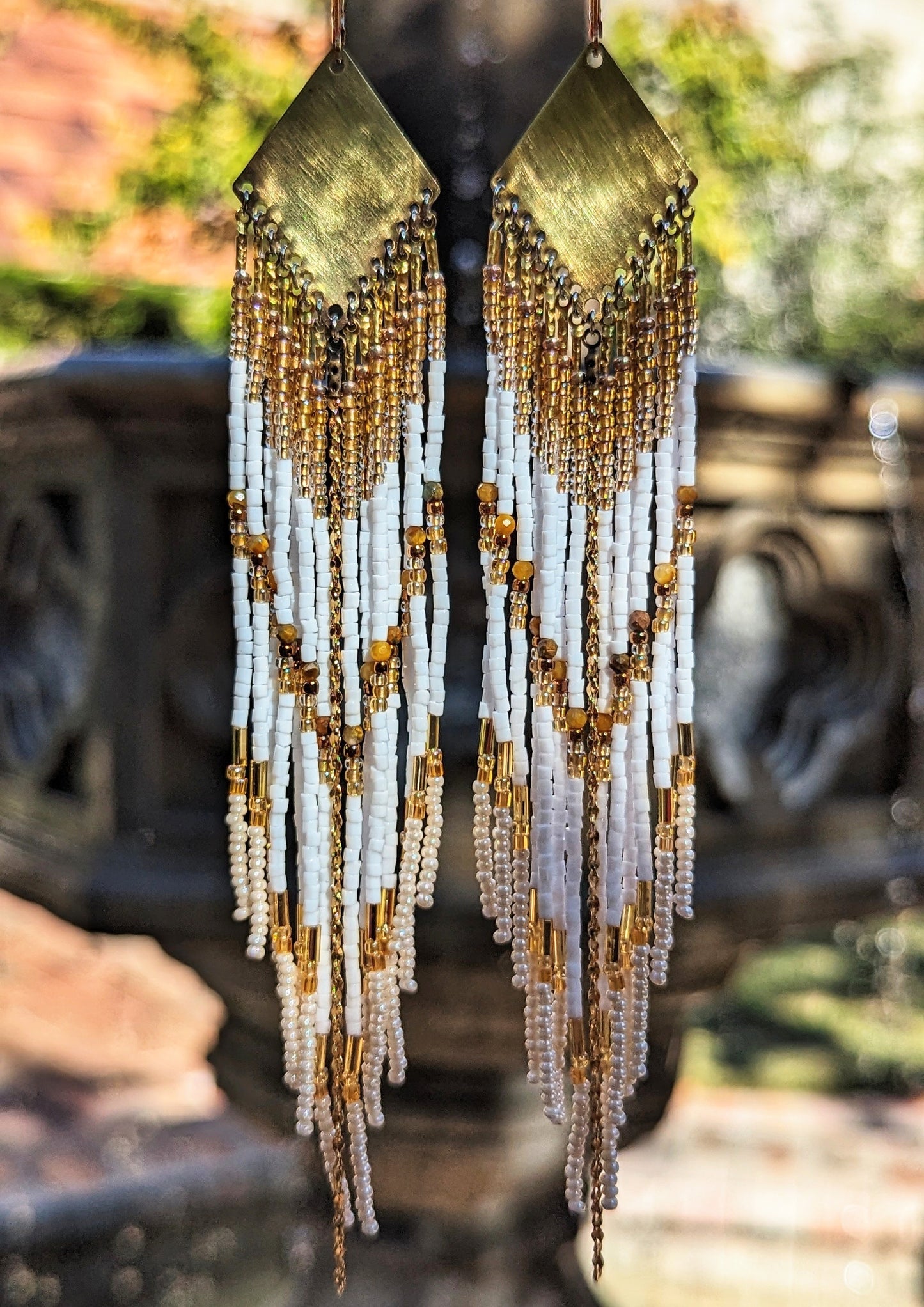 Moon & Milk - Boho beaded earrings featuring white and gold beaded strands cascading from brass geometric plates, displayed in natural outdoor light.