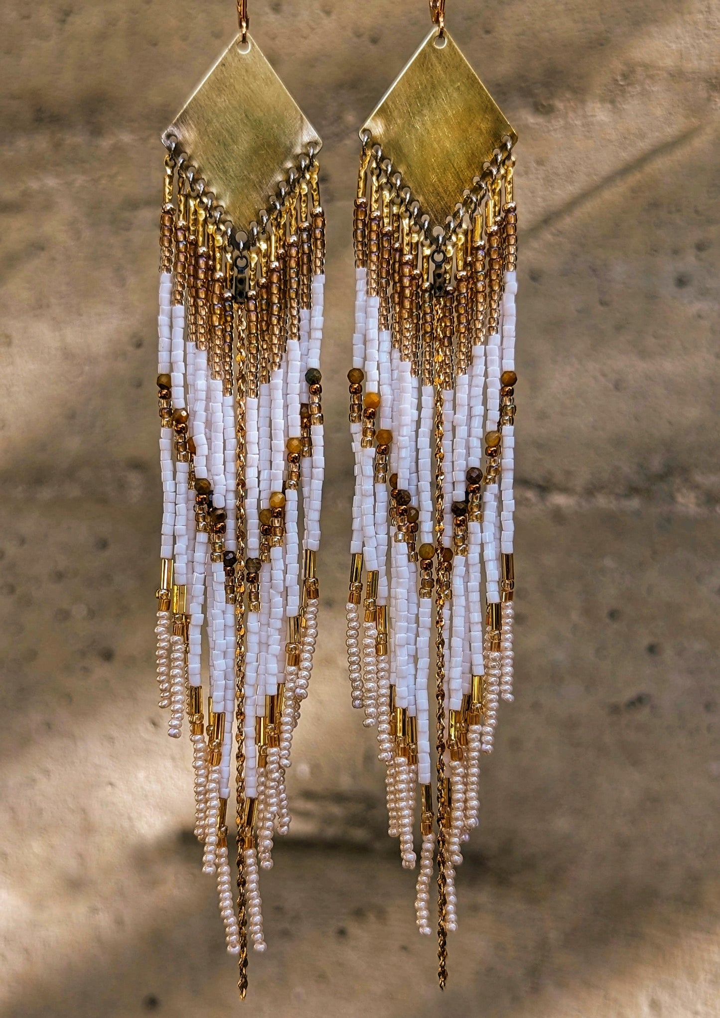 Moon & Milk - Boho beaded earrings featuring white and gold beaded strands cascading from brass geometric plates, displayed in natural outdoor light.