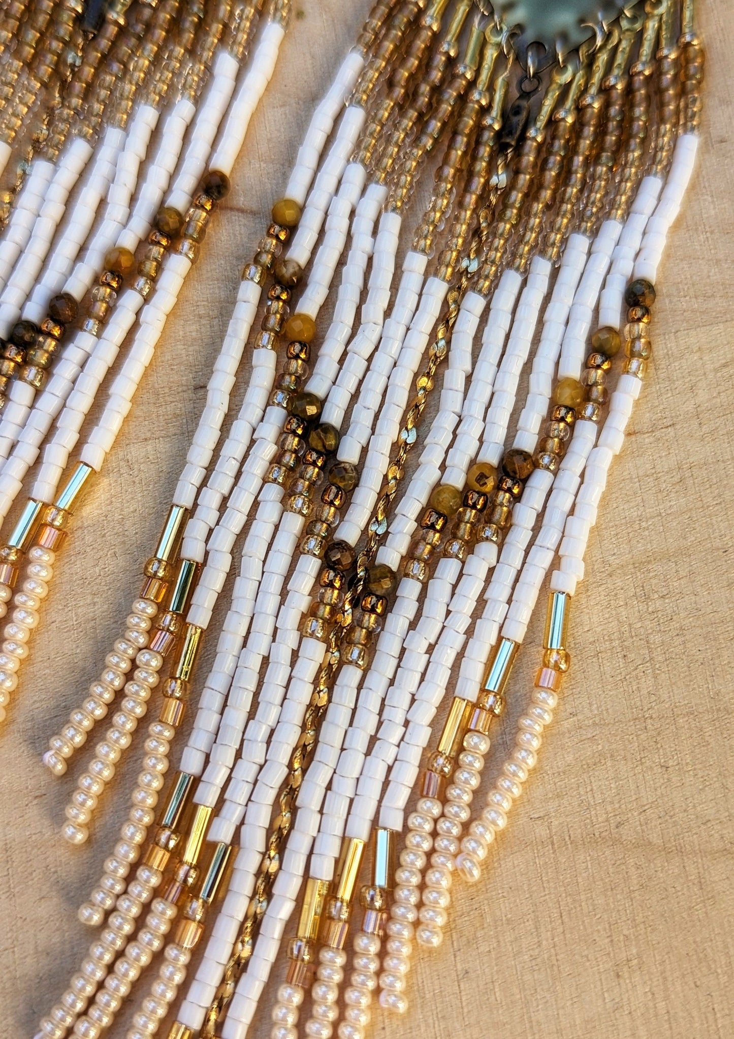 Moon & Milk - Close-up of handcrafted beaded earrings with white and gold beads, cascading in long, elegant strands from brass geometric plates, offering a bohemian style.