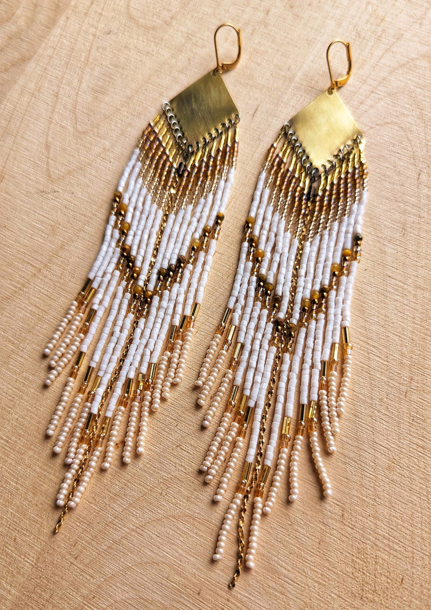 Moon & Milk - Close-up of handcrafted beaded earrings with white and gold beads, cascading in long, elegant strands from brass geometric plates, offering a bohemian style.