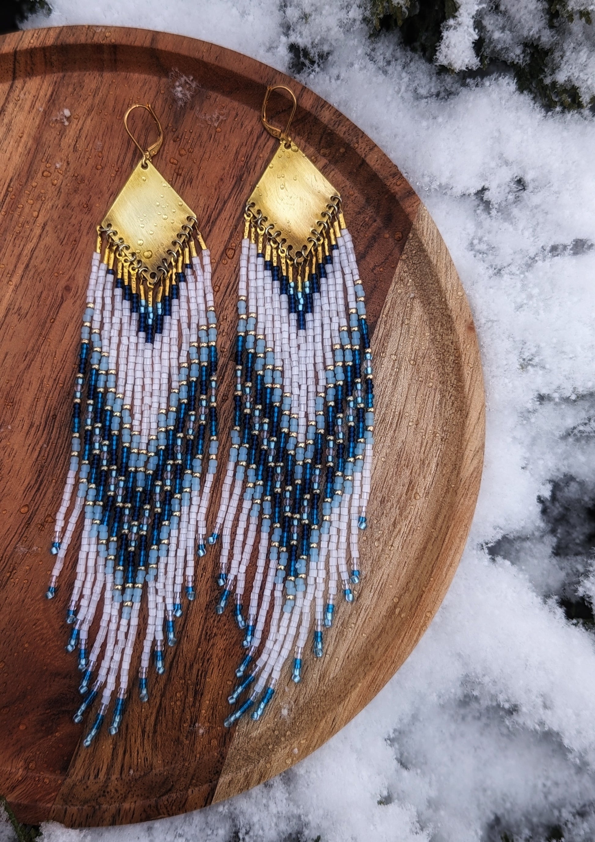 Seed bead earrings with white and blue beaded strands in a gradient pattern with a diamond-shaped golden brass  charm.