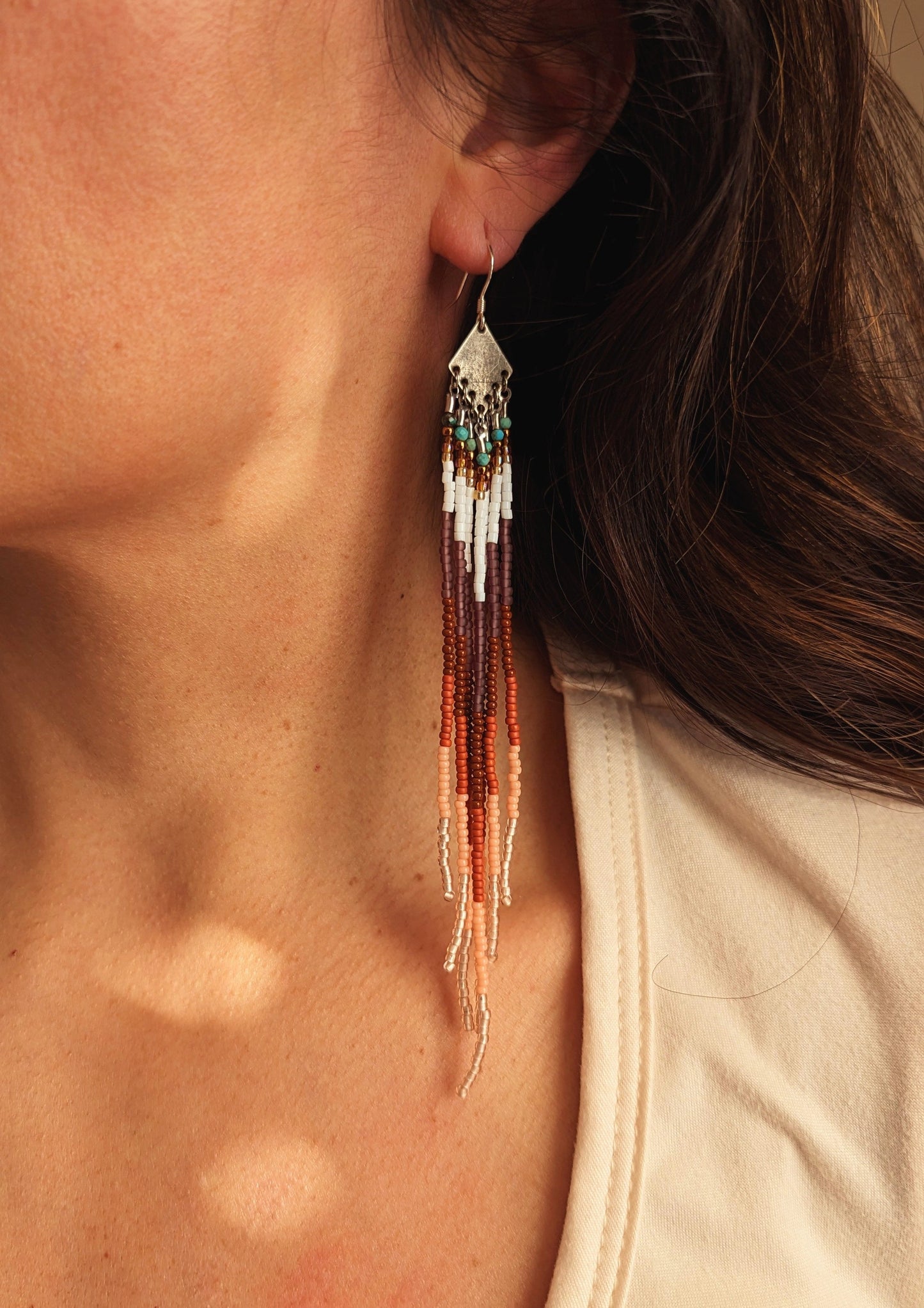Moon & Milk handcrafted earring with soft beaded strands in rust, cream, white, and turquoise tones hanging from a silver diamond-shaped finding.