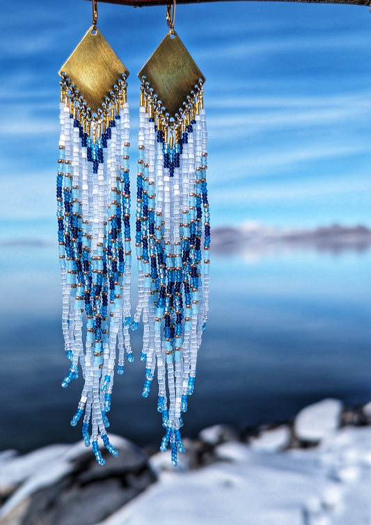 Seed bead earrings with white and blue beaded strands in a gradient pattern with a diamond-shaped golden brass  charm.