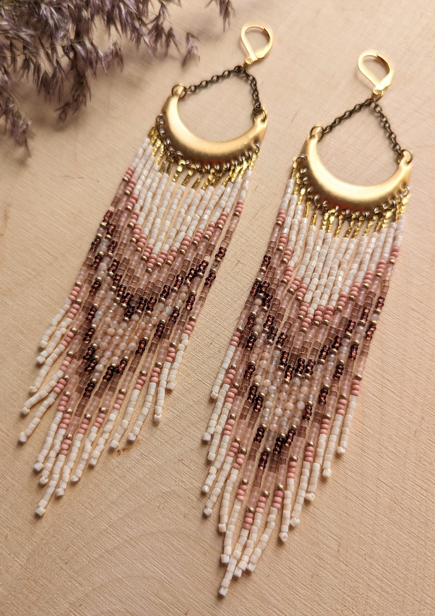 Boho-inspired beaded earrings with a brass crescent, featuring soft pink, cream, and brown beads arranged in a chevron pattern for a natural, earthy look.
