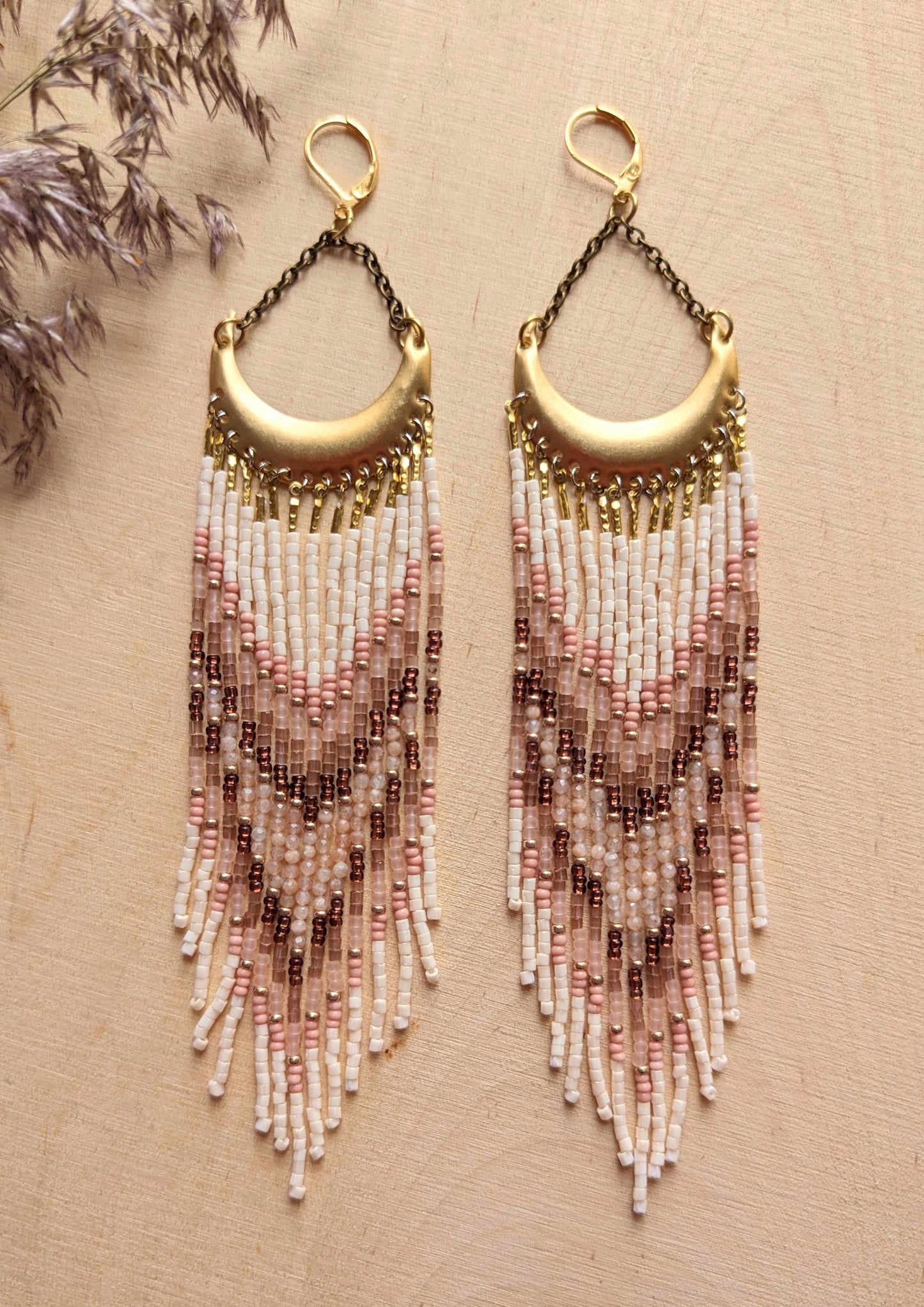 Boho-inspired beaded earrings with a brass crescent, featuring soft pink, cream, and brown beads arranged in a chevron pattern for a natural, earthy look.