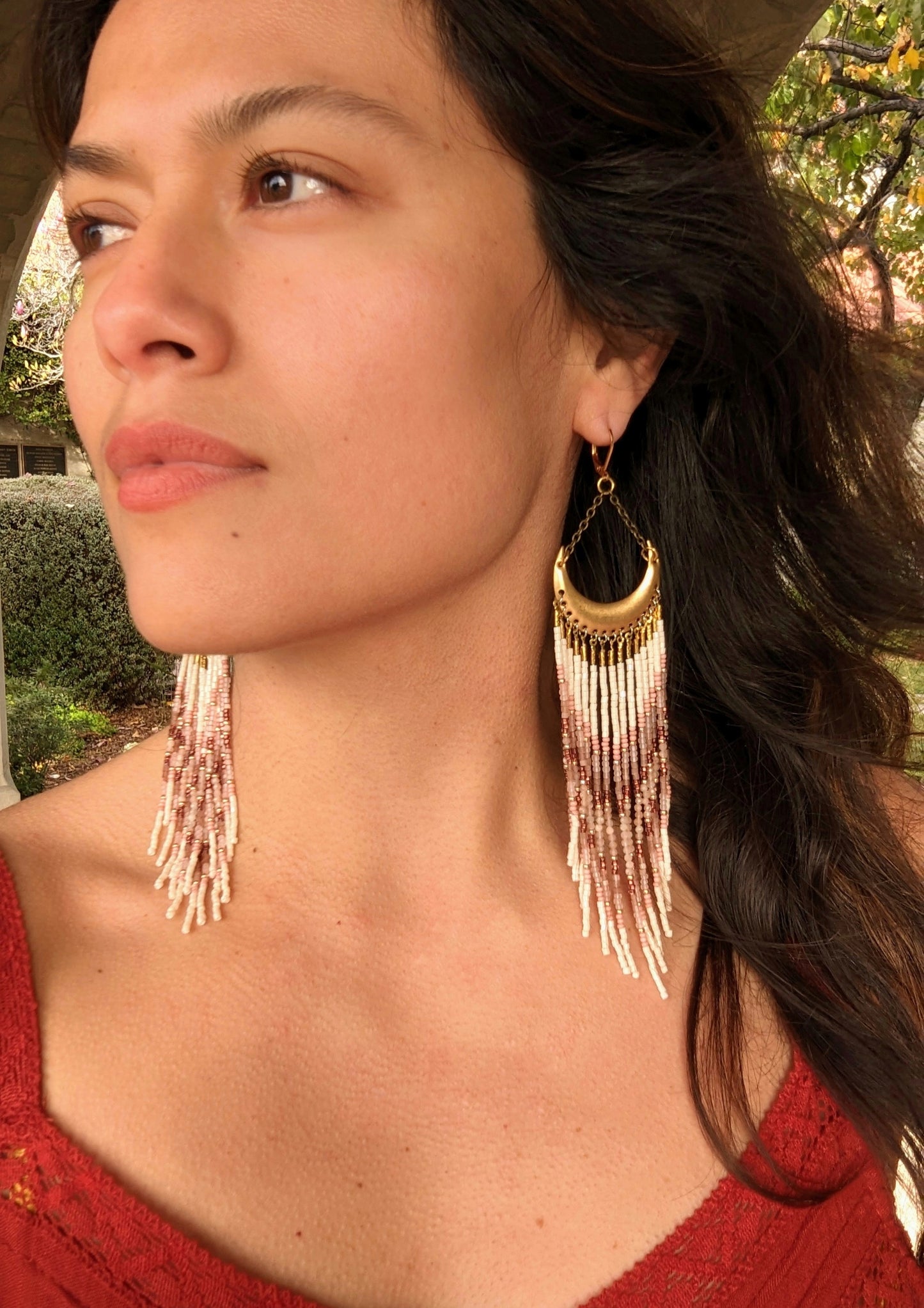 Model wearing boho beaded earrings with a brass crescent, featuring pink, cream, and brown beads in a chevron design, perfect for a natural, earthy look.