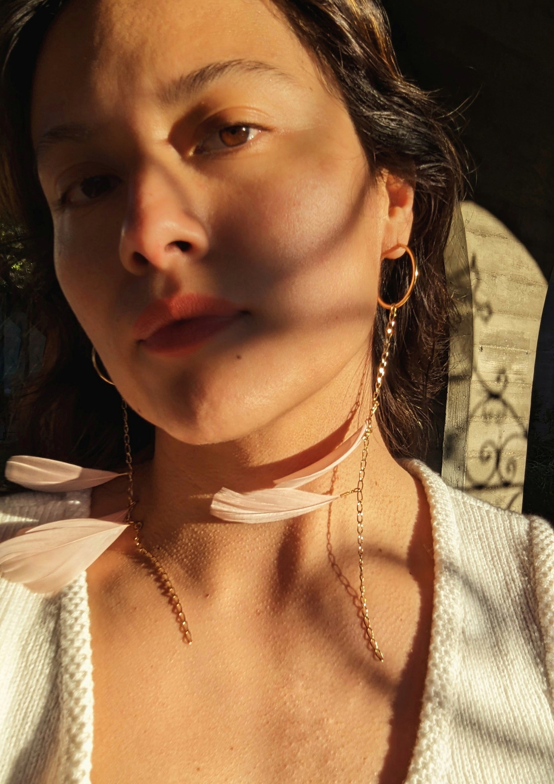 Close-up of a woman wearing Moon & Milk’s blush pink feather earrings with gold chain detail, glowing in golden-hour light.