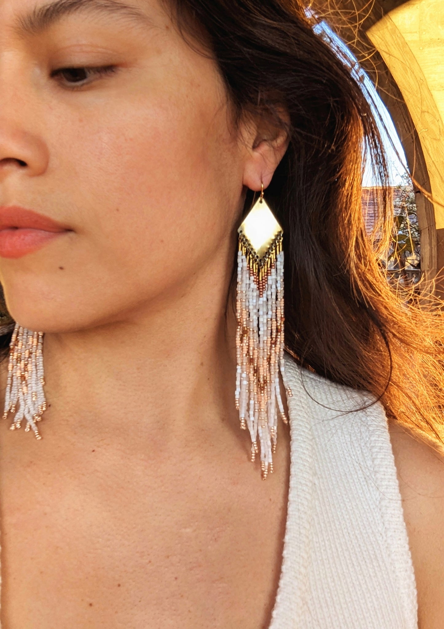 Modeled on a person, these seed bead earrings add a soft, elegant glow that complements the warm, earthy tones of the beads. The golden centerpiece reflects light, enhancing the intricate pattern and bringing a sophisticated sparkle.- Moon & Milk